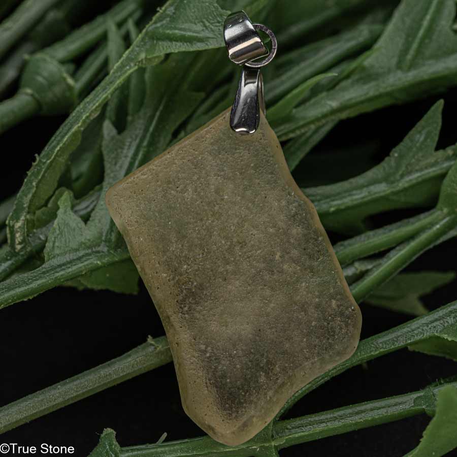 リビアングラスは、今からおよそ2900万年前、北アフリカのリビア砂漠に降り注いだ巨大隕石の衝突によって生まれた、まさに“宇宙と地球の融合”とも言える神秘的な天然ガラスです。 この衝撃によって大地は一瞬にして1600℃を超える超高温状態となり、地表の珪砂が瞬時に融解・冷却され、ほぼ純粋な二酸化ケイ素（SiO2）の塊、それが「天然シリカガラス」、すなわちリビアングラスとして結晶化しました。 これは地球上のどんな火山岩や天然石とも比較にならない、まさに宇宙的スケールの自然現象によってのみ創り出される“地球外の産物”と言えます。 リビアングラスは古代エジプトにおいても特別な素材として扱われており、 ツタンカーメン王の黄金のマスクとともに出土した胸飾りには、 このリビアングラスがスカルベ（甲虫）として用いられていることで知られています。 「数千万年前」の隕石衝突によって生まれた素材が、「数千年前」にはすでに人の手によって「特別な石」として選ばれていたことは、 リビアングラスの歴史的価値を物語るエピソードのひとつと言えるでしょう。 本品は、研磨や成形を一切行っていない原石をそのまま使用し、リビアングラス本来の形状や質感を活かしたペンダントトップとして仕立てています。 自然が作り出した凹凸や不規則な輪郭は、同じものが二つと存在しない一点物ならではの魅力です。 また、淡いシャンパンゴールドの色合いは、光の当たり方や背景によって表情を変え、原石ならではの静かな存在感を感じさせてくれます。 本品はリビアングラスという素材を、日常の中で気軽に身につけて楽しんでいただける一品です。 原石由来の素朴さと、宇宙起源のロマンを併せ持つペンダントトップとしておすすめいたします。 ※本品にはお写真の宝石鑑別書は付属しておりません。 ご希望の場合、別途有料にて宝石鑑別書の作成が可能ですのでお気軽にご相談ください。 尚、鑑別書作成には約10～14日（営業日換算）ほどお時間を頂戴いたします。 【一点物】お写真に写っている商品をお届けします 素材　ステンレス 産地　リビア砂漠 全長（バチカン含む）：約38mm 【原石サイズ】 縦：約29mm×横：約22mm×厚さ：約5.9mm 重量：約3.3g 【True Stone 天然石の真実】ブログ