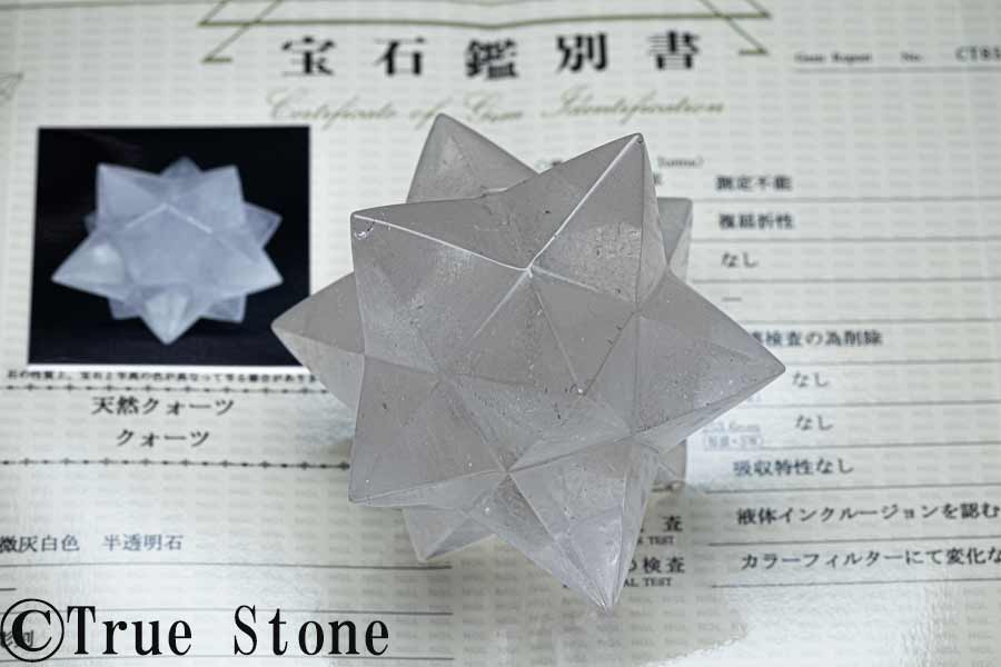 アステロイド・12角マカバスターについて 本品は、12方向に鋭く伸びる頂点を持つ、アステロイド型の天然クォーツです。 一般的なマカバスターは、2つの正四面体を上下逆向きに組み合わせたような星型正四面体として知られ、立体的な六芒星、または神聖幾何学を象徴する形として親しまれています。 それに対し本品は、通常のマカバスターよりもさらに多くの頂点を持つ、12角の星型立体です。 見る角度によって表情が大きく変わり、正面・側面・斜め上など、どの方向から眺めても複雑で美しい幾何学模様が浮かび上がります。 「アステロイド」とは、星や小惑星を思わせる多方向の尖ったフォルムに由来する呼び名で、天然石の研磨品では、立体的な星型カットを表す名称として使われることがあります。 鉱物名ではなく形状を表す呼称ですが、本品のように12方向へ頂点が広がる大型カットは存在感があり、インテリアストーンやコレクション品としても非常に見応えがあります。 【一点物】ブラジル産 天然クォーツ 12角マカバスター／アステロイド ブラジル産の天然クォーツを立体的な星型に研磨した、迫力ある大型アステロイドです。 一般的な小型のマカバスターとは異なり、本品は12方向に鋭く伸びる頂点を持つ、存在感のある造形が魅力です。 最高部で約90mm、重量は349.44g。 手のひらに乗せてもずっしりとした重みがあり、インテリアストーン、浄化用アイテム、コレクション品としても非常に見応えがあります。 透明感は完全な無色透明タイプではなく、微かにグレーを帯びた半透明の質感です。 内部には天然石らしいインクルージョンやクラックが見られ、光の角度によって奥行きのある表情を楽しめます。 天然クォーツならではの内包物や微細な表情も含めて、ひとつの個性としてご覧ください。 12角の立体造形 この形状は、星のように複数の頂点が立体的に広がる神聖幾何学的なデザインです。 見る角度によって印象が変わり、正面・斜め・上部など、どの方向から見ても美しいシルエットを楽しめます。 水晶クラスターやモリオン、天然石ブレスレットなどと一緒に飾っていただくと、空間のアクセントとしても非常に映えるお品です。 本鑑別書付き 本品には、一般社団法人 宝石鑑別団体協議会（A.G.L）会員機関による宝石鑑別書が付属します。 通常の簡易的な鑑別書ではなく、検査項目が詳しく記載された「本鑑別書」タイプとなっております。 鑑別結果は「天然クォーツ／クォーツ」です。 拡大検査では「液体インクルージョン」と記載されており、天然クォーツ内部に見られる特徴が確認されています。 また、蛍光検査では反応なし、分光特性では吸収特性なし、カラーフィルターでも変化なしと記載されています。 液体インクルージョンについて 本鑑別書の拡大検査では、「液体インクルージョンを認む」と記載されています。 液体インクルージョンとは、水晶が地中で成長する過程において、水を主体とする流体が結晶内部の微細な空間に閉じ込められたものです。 いわば、水晶が形成された時代の環境を内部にとどめた、天然クォーツならではの特徴のひとつです。 古い地質時代の水を主体とした流体が、水晶の中に静かに閉じ込められていると考えると、天然石としての魅力をより深く感じていただけます。 鑑別書付きのため、天然石としての確認が取れた状態で安心してお求めいただけます。 サイズ・重量 最大：約90mm 重量：約349.44g 産地：ブラジル 鑑別結果：天然クォーツ／クォーツ 付属品：宝石鑑別書 ご確認ください 本品は天然石を研磨したお品です。 天然由来のインクルージョン、クラック、微細な研磨痕、表面のわずかな凹凸などが見られる場合がございます。 また、先端部分は形状上デリケートですので、お取り扱いの際は落下や衝撃にご注意ください。 【一点物】お写真に写っている商品を発送致します。 鑑別書ブログ ブログ True Stone 天然石の真実