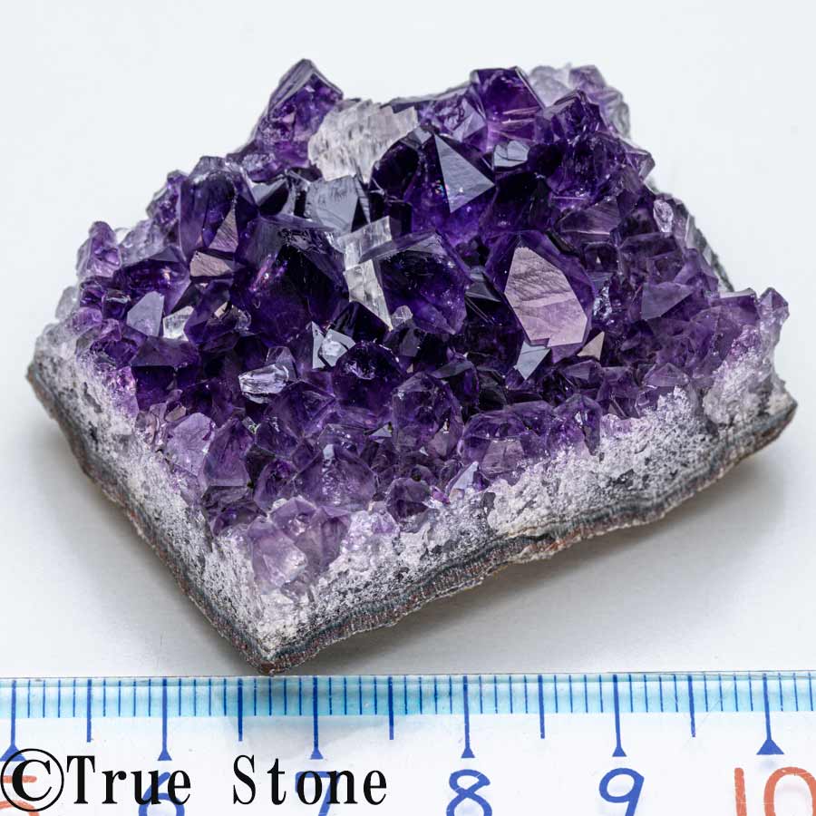 アメジスト アメジストは、和名を「紫水晶」といい、水晶の一種です。 石英（クォーツ）の中で紫色をしたものをアメジストと呼びます。 淡い紫色のものから、深く濃い紫色のものまであり、産地や結晶の状態によって雰囲気が大きく変わります。 ・自然が生み出した紫色 アメジストの紫色は、結晶中に含まれる微量の鉄分などが関係しているとされています。 同じアメジストでも、色の濃さ、透明感、結晶の大きさ、輝き方には違いがあり、それぞれに個性があります。 ・古くから親しまれてきた天然石 アメジストは古くから装飾品やお守りとして用いられてきた、歴史のある天然石です。 落ち着いた紫色は上品で神秘的な印象があり、現在でもアクセサリー、原石、クラスター、ジオードなど、さまざまな形で人気があります。 ・水晶ならではの美しさ アメジストは水晶の一種で、ガラス質の光沢があります。 結晶面に光が当たると美しく輝き、紫色の濃淡や透明感を楽しむことができます。 ・直射日光にはご注意ください アメジストは長期間強い直射日光に当て続けると、色が薄くなる場合があります。 保管や展示の際は、直射日光の当たる場所を避けてください。 アメジストのスピリチュアルな意味合い アメジストは古くから、心を落ち着かせる石、癒しをもたらす石として親しまれてきました。 深く落ち着いた紫色は、精神性や直感力を象徴するとされ、持ち主の心を穏やかに整える石ともいわれています。 ・心を落ち着かせる石 アメジストは、不安や緊張を和らげ、冷静な判断を助ける石とされています。 感情が乱れやすい時や、気持ちを落ち着けたい時にそばに置く石としても人気があります。 ・癒しと安らぎの象徴 美しい紫色の輝きは、見る人の心に安らぎを与えてくれるような落ち着いた雰囲気があります。 寝室やリビングなど、リラックスしたい空間に飾る石としてもおすすめです。 ・直感力や精神性を高める石 アメジストは、直感力や精神性を高める石ともいわれています。 古くから瞑想や祈りの場にも用いられてきたとされ、神秘的な紫色が静かな集中を促してくれるような印象を与えます。 ・大切な人との絆を深める石 アメジストは「愛の守護石」と呼ばれることもあり、大切な人との絆を深める石としても親しまれています。 恋愛だけでなく、家族や友人との穏やかな関係を願う石としても人気があります。 ※天然石の意味合いや効果には諸説あり、感じ方には個人差があります。 ・ウルグアイ産アメジストの特徴 ウルグアイ産アメジストは、濃く深い紫色が魅力のアメジストです。 ブラジル産のアメジストに比べると、明るい紫色というよりも、深みのある濃紫色から黒みを帯びたような重厚な色合いを見せるものが多く、落ち着いた高級感があります。 ・細かな結晶が密集した美しい輝き ウルグアイ産アメジストは、細かな結晶が密に集まって形成されることが多く、クラスターやジオードでは、表面にびっしりと結晶が並ぶ美しい姿が見られます。 光を受けると結晶面が細かく輝き、濃い紫色の中にも透明感や奥行きを感じられます。 本品は、ウルグアイ産のアメジストです。 ウルグアイでは、北部のアルティガス県周辺がアメジストの名産地として知られており、玄武岩中の晶洞内に美しいアメジストが形成されます。 濃く深い紫色と細かな結晶の輝きが、ウルグアイ産アメジストならではの大きな魅力です。 カルサイトが共生します。 一点物 本品は一点物として掲載しております。 写真の商品をそのままお届けいたしますので、色合い、結晶の形、サイズ感、母岩の状態などを写真にてご確認ください。 【商品詳細】 産地：ウルグアイ 縦：約21mm 横：約44mm 厚さ：約34mm 重量：約48g 鑑別書ブログ True Stone 天然石の真実
