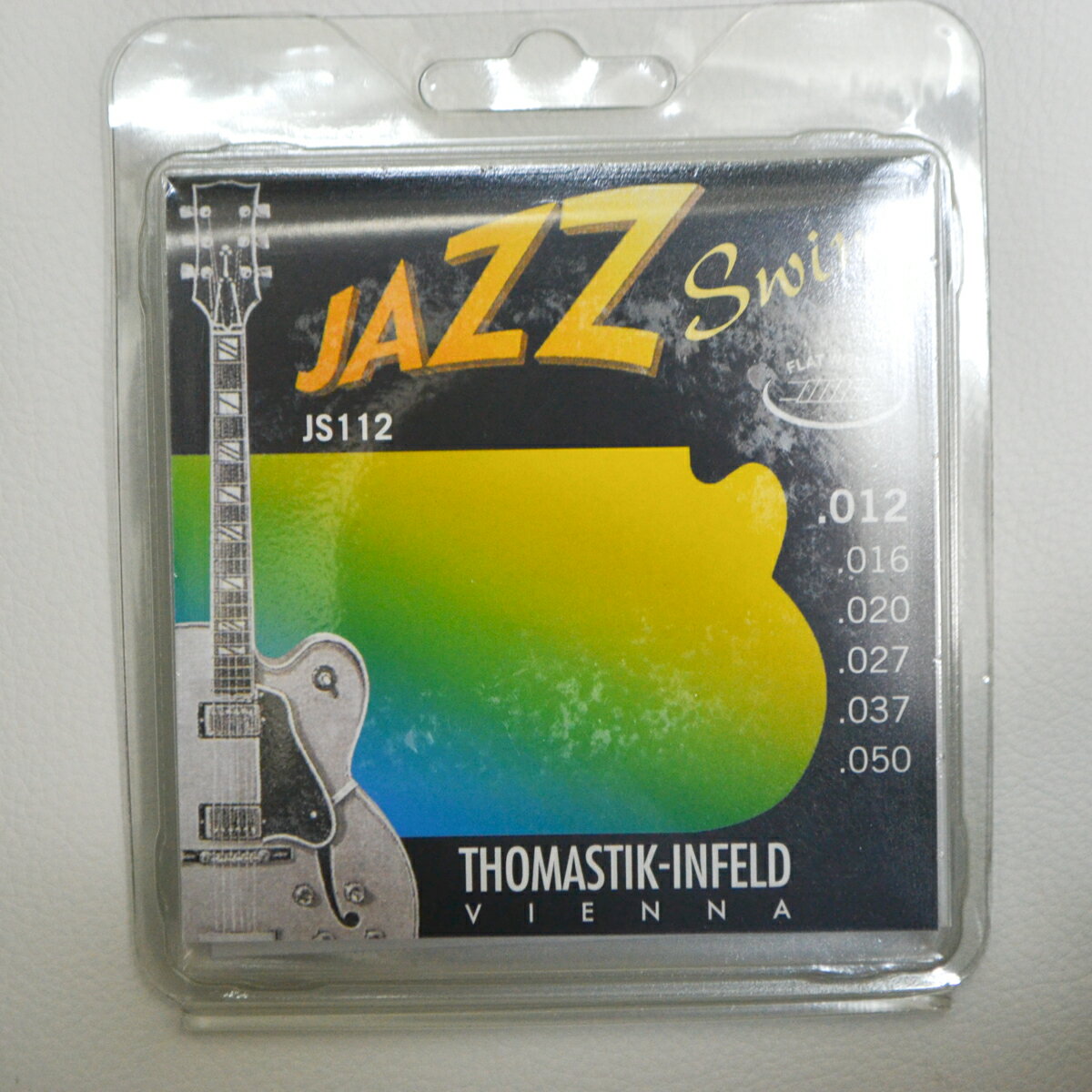 Thomastik-Infeld JS-112 Jazz Swing 12-50 Thomastik社が作り出したフラットワウンドジャズギター弦は多くの音楽家の間に口コミで広がり、いまや唯一無二の伝説的な存在として認められるようになりました。 本当のフラットワウンド弦（決してグランドワウンド＝削り出しや、プレスワウンド＝圧縮ではないもの）とは時間と技術を惜しまず、ガラスの表面のように磨きこまれたリボン状のニッケルを丸い芯線に巻いていったものです。 Thomastik社が長年のクラシック弦の製造で持ちえた技術を採用してあり、芯線と巻き弦の間にわずかな隙間もなく密着しているため、振動を可能なかぎり自然な状態にすることができます。 この結果がトラディショナルなジャズプレイには欠かすことのできないオーバートーンを完璧なバランスで生み出すわけです。 -ゲージ- 1st(E) Plain Steel .012 2nd(B) Plain Steel .016 3rd(G) Nickel Flat Wound .020 4th(D) Nickel Flat Wound .027 5th(A) Nickel Flat Wound .037 6th(E) Nickel Flat Wound .050 -Thomastik-Infeld- Thomastik-Infeld（トマスティック・インフェルト）社は、第一次世界大戦が終了した翌1919年に、「音楽の都」オーストリアのウィーンで、バイオリンの製作家Dr. Franz Thomastik（フランツ・トマスティック博士）と技術者のOtto Infeld（オットー・インフェルト）が共同開発して設立し、バイオリン族だけでなく、ギター弦の総合メーカーでもあります。 弦だけの振動は単に空気を切るブーンと言う音だけですが、その弦の振動が楽器本体を共鳴させて、その楽器固有の楽音を発生させています。 トマスティックはその総体的な関連を知悉しており、倍音の構成、イントネーションの完全性などを追求して、素材を深く研究・開発し、製造工程を完璧に整えて、最高品質のギター弦を提供するだけではなく、プロギタリストとの密接なコラボレーションが製品のコンセプトを確かなものにしています。 ※画像はサンプルです。モニターの発色の具合等により、実際の物と色味が異なる場合がございます。 予めご了承下さいませ。 その他は こちら→