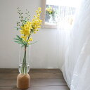 商品情報使用花材ミモザサイズ高さ・・・ガラス花器底面からトップの花まで　　　約38センチ前後ガラス花器　　　　　　20Hx5W　(口径)Φ5.0cm注意点・本製品は食べ物ではありません小さなお子様が口に入れないようにご注意下さい変色や変形の原因となります・アートフラワーは特性上、多少のエッジのほつれ・色落ち・シワ等はございます。 仕入の後、、状態が良いものを厳選して発送させていただきますので 「ほつれ・色落ち・シワ」等は不良品ではございません。 返品の対象にはなりませんので、御了承くださいませ。・アトリエでひとつひとつお作りしていますハンドメイドです。同じ様な花材で同じ様に制作させていただきますが全く同じ物と言うわけにはいかない場合があります。ご理解お願いいたします。・お品の撮影は色加工などせずに撮っておりますがモニターによりお色の映りに相違がある場合が御座います。個人の主観でのお色の相違などもあるかと思いますので、気になる点はどうぞご質問下さい その他ギフトで贈られる場合はセロファンラッピングとリボンを施して発送させて頂きます。メッセージ等、代筆で宜しければ承ります。心を込めて代筆させて頂きます。ミモザ　魔法の水　マジカルウォーター　インテリア　ギフト ミモザ　魔法の水　マジカルウォーター　インテリア　ギフト　 水替え不要の魔法の水 固まってこぼれない 水替え不要のマジカルウォーター！一年中飾れます 春色のポップなイエローミモザのウォーターアレンジです。ころころと可愛らしいフォルムが愛らしく、華やいだ雰囲気になります。自然光の中に置くと、まるで本物のようにクリアで綺麗なお水にみえるマジカルウォーターはお手入れ不要でずっとそのまま長く飾って頂けます。画像後半のリアルなミモザのドライフラワーも販売中です♪●●●〜マジカルウォーターとは〜●●●本物のようにクリアで綺麗なお水にみえるシリコン素材の人工水です。倒しても零れることもなく水替えも不要です。この状態のまま、ずっと楽しんで頂けます。興味はあったけど、大きなものは抵抗がある方や小さなスペースに飾りたい方など。このままリビングや玄関、インテリアとして飾って素敵です。 生花の手入れが苦手な方にもこれなら楽!様々な事情で、生花を贈りたくても出来ない時など。●生花のお手入れが苦手な方に●花粉アレルギーで生花が置けないご家庭に●花の匂いが苦手な方に●渡すのに時間がかかってしまうため生花では困る●事前に用意しておきたい●数日で終わらずにずっと飾って置きたいメッセージカードもお付けできます。お気軽にお申しつけ下さいませ 3