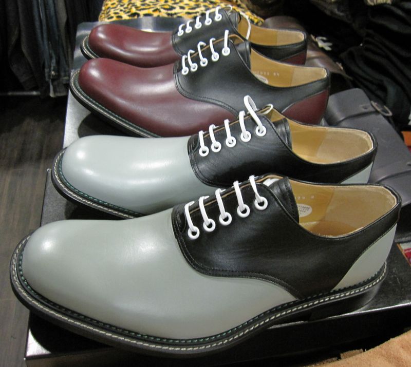 Color : GRAY /　WINE Size :　 8, 8ハーフ, 9 日本ではサドルシューズの俗称で親しまれている、甲の部分に馬の鞍(サドル)形の別革を貼付けた紐結び式の短靴です。正式名称を「サドル オックスフォード」と呼びます。 古くは19世紀の終わり頃にイギリスで作られ、後にアメリカに伝わった際、俗に「コンビサドル」と呼ばれる2色のレザーを使用した形が学生靴やダンス用のシューズとして1950年代に大流行しました。鳩目及び靴紐をホワイトにする事で、より一層当時のトラディショナルな雰囲気を出しています。 縫製はマッケイ製法を採用しているため軽量に仕上がっており、足運びも良く長時間履いていても疲れにくくなっています。コバ部分は1950年代当時のディテールを思わせるダブルコバにしており、内側のステッチ糸は「元々黒かった糸色が、経年変化により退色した」というヴィンテージシューズの風合いが出ています。また、プラスチックソールと相まってより一層クラシックな雰囲気に仕上がっています。ライニングにはナチュラルカラーのピッグスキンを使用しており、足入れも良く靴下への色移りを防いでくれます。 ボタンダウンシャツにチノパンやジーンズを合わせたスクール調のコーディネイトから、ジャケットにスラックスを合わせたアダルトな雰囲気の着こなしまで、様々なシーンで活躍してくれる一足です。　