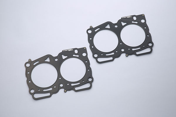 車メーカーSUBARUスバル車種WRX STI年式H16〜 (2004〜)エンジンEJ257適合備考海外仕様品番1361101071品名ヘッドガスケット 101.2-0.7mmボア径(Φ)101.2厚さ(mm)0.7材質メタル構造スーパーグロメット備考2枚セット納期についてメーカー在庫があれば3〜4営業日、欠品時は1ヶ月〜お時間がかかります。お急ぎの場合はご注文前に必ず在庫確認をお願い致します。※納期が遅い等によるキャンセルは一切お受けできません。注意事項※ こちらの商品はメーカー直送になります。※ お客様の見落としや確認ミスでのキャンセル・交換・返品は一切お受けできません。※ 商品画像は代表車種の物です。車種毎に形状は異なります。※ 適合情報は随時更新しておりますが、告知なくメーカー側にて更新される場合がございますので、必ずご注文前にメーカーホームページにて最新の適合表をご確認頂ますようお願い致します。TOMEI POWERED GASKET ガスケットヘッドガスケットEJ25FEATURE / SPEC■ スーパーグロメット採用純正品の素材は非メタル系。構造がグロメットタイプでシール性能が不足しています。TOMEIヘッドガスケットシリーズは信頼性抜群のスーパーグロメットタイプを採用することにより、シール性能が向上します。 スーパーグロメットタイプビード構造と金属グロメットのデュアルシール方式により、冷却水やオイルシールはもちろんボア外周のガスシール性を最大限に向上する。 ■ ステンレス材の熱伝導＆強度追従性が良くしなやかな材質であるSUS301をビード構造表板に採用。優れた耐熱性、耐久性を有しヘッド及びシリンダーの熱を効果的に冷却水に伝え冷却する事が可能な為、局部的に高温にならないので、吹き抜けが起こりにくいのです。また、ステンレスは引っ張り強度にも強い為、繰り返し起こるシリンダーの変形に対してもビードが追従することで吹き抜けに対して有利であり、ヘッドとブロックの結合剛性を高く出来ます。ヘッドとブロックの結合が強固だと、エンジン全体の剛性が増し、ねじれや曲げを低減する事ができ、また運動軸受け部の耐久性が向上します。■ 専用リブ設計 リブを高くするとガスシール性は向上しますが、その分、周辺の冷却水やオイルのシール性が低下してしまいます。そのためパワーアップを計ると冷却水やオイルの漏れが発生することがあります。TOMEIではスーパーグロメットタイプの採用と、リブ高さを設計から見直すことにより、全体の面圧を高く、均一に保ちシール性を向上させました。 ■ マーキングについて TOMEI製のメタルヘッドガスケットには全てに機種・ボア・厚み・TOMEIPOWERED INC. ロゴがマーキングされています。ロゴなどを十分確認され、東名パワード製と称す模造品や類似品にご注意ください。