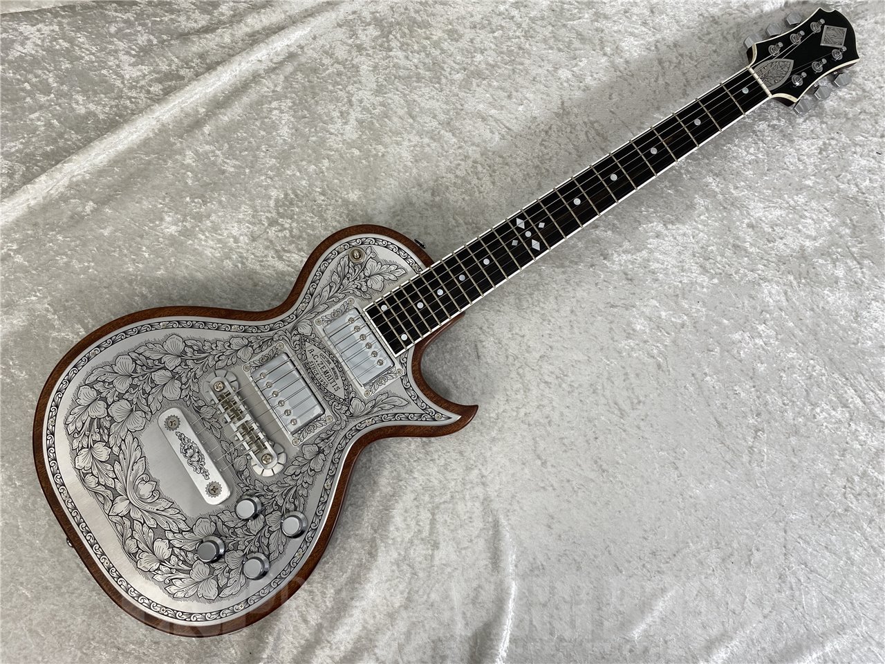 英国発祥のゼマイティスらしさや伝統的なデザインを前面に出ししつつ、最前線でプレイするギタリストやギター・テクニシャンたちへの徹底的なヒヤリングを重ね、現代のプレイヤーが求める要素を注入したモデルに仕上がっています。 ゼマイティスより、トップに彫金装飾を用いたメタル・フロント・モデル「MFG-AC-24」が登場しました。 ゼマイティス最高級モデルの生産工場と同じ工場で製作した、ハイグレードなモデルです。 ウェストのくびれが大きいシングル・カッタウェイのボディー・スタイルで、ボディーとネックに厳選されたアフリカン・マホガニー、フィンガーボードはエボニーを使用しています。 635mmのスケールで、セット・ネック・ジョイント、ミディアム・サイズの24フレット仕様です。 ボディー・トップのアルミ合金のプレートにゼマイティスらしいリーフ柄の彫金装飾を全面に加え、伝統を示す「A.C.ZEMAITIS SINCE 1955」の文字が刻まれたデザインなどクラシックなルックスが特徴です。 ゼマイティス・オリジナルのアルミ合金を使用したブリッジ＆テイルピースを搭載し、ゼマイティス独自のトーンを生み出す要素となっています。 同様にアルミ合金を用いたヘッドのダイアモンド・エンブレム、トラスロッド・カバー、テイルピースやピックアップ・リングをはじめ、アウトプット・ジャック・プレート、コントロール&amp;スイッチ・バック・プレートに至るまで彫金を施しています。 ピックアップは、メタル・カバード・タイプのDragon Classicハムバッカーを2基搭載、コントロールは定評のあるCTSポットを使用し、各ピックアップ・ヴォリュームと各ピックアップ・トーンのレイアウトです。 スイッチクラフト製の3ウェイ・ピックアップ・セレクター・スイッチを備え、トーンのキャパシターはオレンジ・ドロップを使用しています。 さらに信頼性の高いゴトー製のチューナーを使用しています。 フィニッシュはラッカーを使用し、カラーはナチュラルです。 ハードケースが付属します。 ■主な仕様 Body Top：Duralumin Body Back：Select African Mahogany Neck：Select African Mahogany Neck Joint：Set Neck Nut Width：43mm (1-11/16") Nut：：Bone Fingerboard：Bound Ebony Scale：635mm (25") Frets：24 Medium Neck Pickup：Dragon Classic Neck Bridge Pickup：Dragon Classic Bridge Radius：305mm (12") Controls：2 volume, 2 tone, 3-way toggle Tuners：Gotoh® SG301-01-Chrome Finish：Lacquer Protection：Hard Shell Case Strings：Nickel Plated Steel (.010, .013, .017, .026, .036, .046) Color：Natural ※こちらの商品は実店舗BIGBOSSお茶ノ水駅前店でも販売しております。商品が販売された場合にはサイトからすぐ商品削除をするよう心がけておりますが、場合によってはすでに売却済みの場合もございます。 あらかじめご了承下さい。【BIGBOSS 8つの安心】当点リペアマンが弾きやすいようにセットアップしてお送りさせていただきます。ご購入後のメンテナンス・セットアップもいつでも無料です！くわしくはこちらをご確認ください。