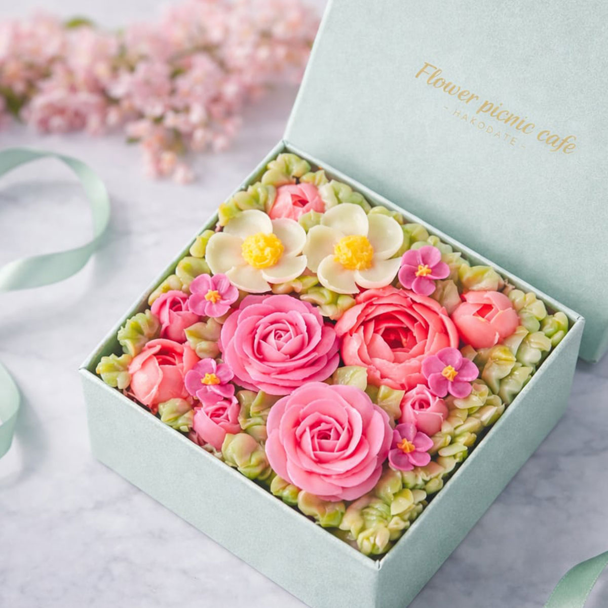 食べられるお花のボックスフラワーケーキ（ブルームガーデン）冷凍 まるで生花のような華やかさと透明感！開けた瞬間に笑顔咲く、北海道産の食べられるお花のボックスフラワーケーキ 商品説明 北の大地、北海道函館市の「flower picnic cafe（フラワーピクニックカフェ）」から、食べられるお花のケーキを産地直送でお届けいたします！ 「食べられるお花のボックスフラワーケーキ」は、ひとつひとつのシーンを特別にする、幸せと可愛さを箱の中に詰め込んだフラワーケーキです。 まるで本物のお花のような華やかで繊細な花びらは、1枚1枚手作業で丁寧に絞ったバタークリーム。特別なレシピでつくったバタークリームは、濃厚なのにあっさりとクリーミー。ふわっと柔らかい口溶けをお楽しみいただけます。 スポンジはバタークリームとの相性を研究し、北海道産の小麦・人参を使用したバタークリーム専用キャロットケーキに仕上げました。 また隠し味のシナモンが味全体に統一感を与え、コーヒーや紅茶、お酒にもよく合います。 “見た目だけじゃない”本当に美味しい、視覚と味覚が一度に満たされる特別なケーキになりました。 お花をそっと優しく包み込む、ミントブルーの専用ボックスに入れてお届けいたしますので、大切な方への贈り物に、特別なプレゼントや記念日・お誕生日に、母の日や父の日に、結婚や出産のお祝いにぴったりな商品です。 ※冷凍便でお届けいたします。 ※産地直送の商品となる為、flower picnic cafe以外の商品との同梱、代引きが出来かねます。 ※内容は事前の予告なしに変更になる場合がございます。 内容量 360g 箱サイズ 縦:13cm×横:13cm×高さ:9cm 原材料名 小麦粉（北海道産）、人参（北海道産）、バター、卵、生クリーム、砂糖、オイル、クランベリー、シナモンパウダー、食用色素（赤色3号、赤色40号、黄色4号、黄色5号、青色1号）（原材料の一部に小麦・乳・卵含む） 賞味期限 冷凍1ヵ月 ※解凍後は翌日までにお召し上がりください。 製造者 北海道函館市元町7-9 株式会社Flower Picnic Cafe 配送のご注意 離島や運送機関が定める特定地域へのお届けを希望される場合、更なる追加代金の発生、配送所要時間の延長、お届け不可のためご注文をお断りさせていただく事がございます。ご心配されているお客様はお電話にて配送の可否をご確認後にお申し込みください。 母の日 誕生日 ケーキ スイーツ お花 記念日 サプライズ 結婚祝い バースデーケーキ かわいい おしゃれ インスタ映え お祝い お取り寄せ お土産 手土産 プレゼント 贈り物 ギフト 北海道 函館 flower picnic cafe