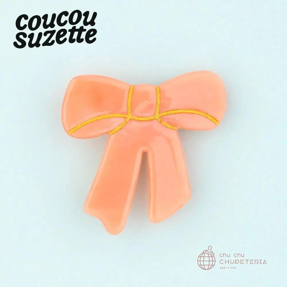 Product:Pink Ribbon Hair Clip ロマンティックなパステルピンクにゴールドのラインが施されたレトロで愛らしいリボンのヘアクリップです。小ぶりながら存在感抜群で、前髪留めやヘアアレンジのアクセントにするだけでなく、シャツの襟元やバッグの持ち手、帽子の飾りとしても活躍します。 &nbsp; Size:&nbsp;約4x4cm Material:&nbsp;セルロースアセテート &nbsp; Important:&nbsp; ・当店はCoucou Suzetteと正式に契約し、正規品のみを扱っている公式販売店です。・塗装のはみ出し、色むら、ドットの付着、気泡の混入、表面の小傷、金属部分のゆがみや変色がある場合がございますが、メーカーの出荷基準に基づき販売いたします。 ・時期により、Coucou Suzetteの刻印に色味が無くなったり、ロゴ自体がCoucouSuzetteから目のマークやその他のマークに変更になる場合がございますのでご注意ください。 🇫🇷Coucou Suzette / ククシュゼットフランス人イラストレーターのジュリエット・マレによって2013年に設立された、パリ発のポップで遊び心あふれるアクセサリーブランドです。カラフルで少しシュールなデザインが特徴で、ブランドの象徴である「目」や「胸」のモチーフ、愛らしい動物などをあしらったヘアクリップ、ソックス、ピンバッジなどが世界中で人気を集めています。SNSを通じて爆発的に広まったその独創的なアイテムは、日常にユーモアと彩りを添えるファッションアイコンとして、幅広い世代から愛されています。コレクターや、プレゼントにも大人気！