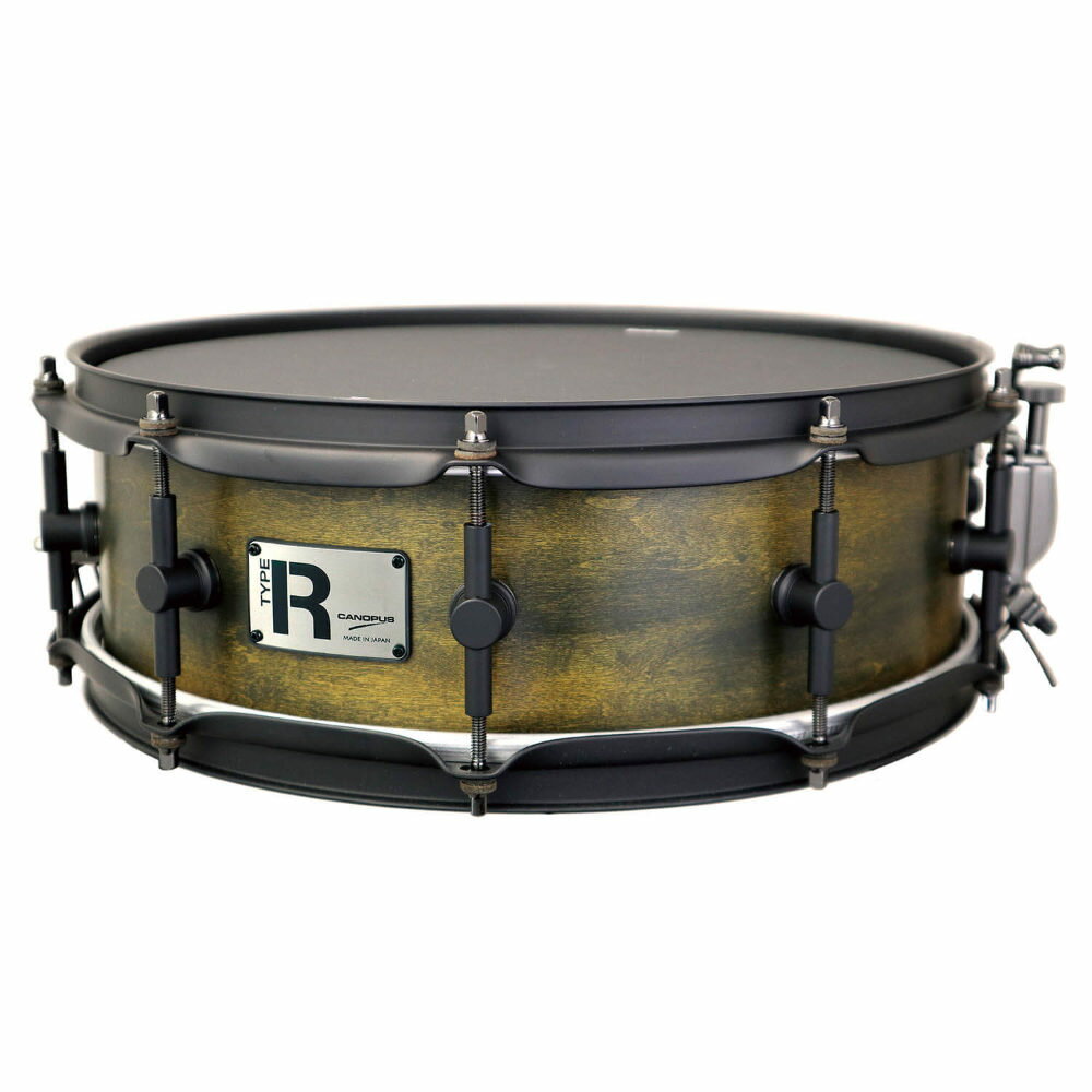 CANOPUS カノウプス Type-R MTR-1450PH-CM 5インチ×14インチ スネアドラムアタック感を核とするブランドコンセプトのもと、現代のミュージックシーンに求められる「抜け」と「コントロールされた倍音」に着目。重量感ある厚胴に頼ることなく、木胴ならではの自然な鳴りを活かしながら、明瞭なアタックと整理された倍音バランスの両立を目指して開発したスネアです。ベースとなる8ply Mapleの優れたレスポンスに、あえてオイルフィニッシュを施すことで、スピード感と豊かな鳴りを最大限に引き出しました。一方で暴れがちなこの組み合わせに対し、マットブラックコーティングを施した倍音を抑制するパーツを併用し、全体のサウンドをタイトにコントロール。さらにBlack Coatedヘッドとの組み合わせにより、粘りつくような芯のある打感を維持しながら、一打一打に確かな響きと優れた音離れを実現しています。荒々しい性格はそのままに、狙い通りに鳴らし切る。まさに“暴れを味方にする”スネアが実現しました。【スペック】・SIZE：14” x 5”・Shell：Maple 8ply 5mm・Color：Rotten Amber Oil・Hoop：Matt Black 2.3mm - 10H・Strainer：CSA20S / CSA21B・Head：asrp Black Coated 1ply/ REMO SA・Snare Wire：CPSS-BB14DR・付属品：無し