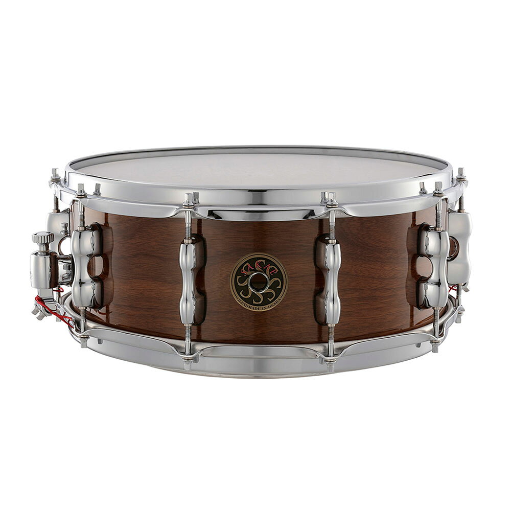 SAKAE OSAKA HERITAGE SD1455WNJ 14インチ×5.5インチ WALNUT SNARE DRUM ウォルナットスネアウォルナット・スネアはドラム界のデリカテッセンです。最高級のウォルナット材を選定し、大阪のラボで熟練の職人の手によって加工することで、広いレンジ、豊かな音量、ウォルナットだけが持つ独特の音色を最大限に発揮しています。非常に独特かつ繊細なサウンドを持っており、あらゆる音楽にマッチします。●シェル7プライ、7.2mmのシェルで、バランスがとれたスネアサウンドを実現しています。豊かで明瞭な中音域が特徴です。●スネアワイヤー太さのあるウルトラハイカーボン製です。一般的なハイカーボンよりも多くのカーボンを含むことで、強度が増し、より速く、シャープなレスポンスを実現しています。●フープJAPAN CUSTOM SNAREには、SAKAEおなじみのMighty Haloが付属します。フープの上端が内側を向いていて、高域倍音を抑えた力強いサウンドを生み出します。●ラグダイキャスト鋳造の強化金属によって上から下への音の伝達が速くなり、シャープな音が得られます。●ストレイナー非常に高感度かつ正確です。プレイヤーが求める繊細なテンションを自由自在に設定することができます。