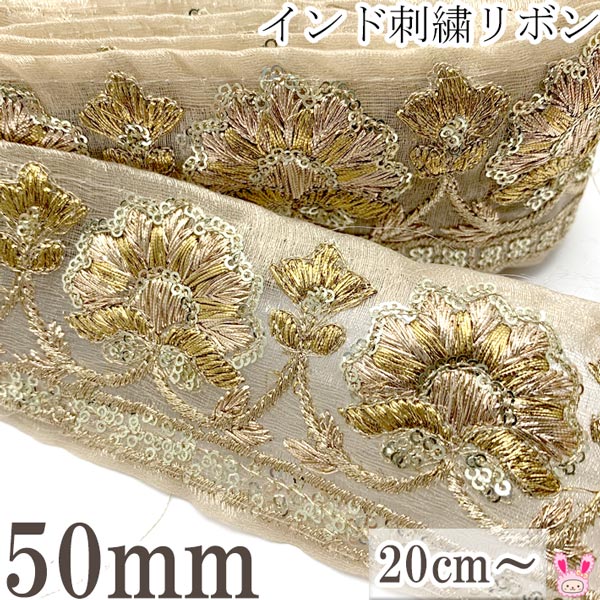 インドの民族的な特徴をもったとっても豪華な花柄インドトリムです！ シースルーのような透け感のある蓮の花が刺繍されています。 細かな輪状のスパンコールと、煌めきを放つ黄金の金糸が美しい。 どこか神聖で、威厳のある風格のデザイン。 婚礼やお祝いなど、特別な雰囲気を追加したいハンドメイドにもおすすめです！ 無地のバッグやポーチにアクセントとして取り付けるだけで、高級感のある印象がプラスされます。 アジアン雑貨やインテリアのハンドメイド、お洋服の襟や袖などリメイクにもオススメです！ 【オーダーカットのご注文について】 オーダーカット（計り売り）での販売です。 約50mm幅リボン、10cmあたりの価格となっております。 ご注文は20cm（数量2）から承ります。 リボンはつながった状態でお届けいたします。 ※数量入力例：20cm→「2」、1m→「10」 注意事項 ・手作りの商品の為幅に数mmの誤差や、刺しゅうが画一的ではない部分があります。 　縫い目が均一でない場合や、ほつれ、パーツの取れがありますが現地の民芸品としてご了承下さい。 ・輸入商品の、少々のキズ・ヨゴレがある場合がございます。 ・入荷時期により、色合いや幅のサイズ・デザイン等にバラツキがでる場合がございます。 ・入荷時期により価格の変動がございます。予めご了承ください。 インド製　Made in India インド刺繍りぼんとは・・・？ カラフルな色やゴールドの装飾を好むのインドの女性が、マハラジャのために金糸を使ってゴージャスなリボンテープに仕上げたのが始まりです。 代表的なチロリアンもインドししゅうの一つ。まるでアート工芸作品のような民族特有の伝統的技法やデザイン。 豪華な刺しゅうを施している為、太めの幅広いリボンが多く、金色の糸や、平丸スパンコール、亀甲ビーズ、輝きが綺麗なデコストーン、インドミラーパーツ、ブレードなどの装飾があしらわれています。 インド古来の伝統工芸のモール糸を使って手刺繍するザリ刺繍や、フリル模様のようなスカラップの刺繍や、大きな蓮のお花柄のロータス刺繍、ボタニカルデザインの植物模様の刺繍、チロリアンテープに多いチューリップ刺繍などりぼんテープのデザイン方法は様々。 下地の生地も様々で、ローシルクと呼ばれるサテンのような光沢のある優しい質感のものや、模様を直接編み込んだシャガード織り、シースルーの透け感がオシャレなチュールメッシュ、高級感のあるベロア素材など種類が豊富。 その上の刺繍は、一つ一つ手作業で縫製された手刺繍や、機械刺繍です。 手触りは、ファブリックリボンならではの、くったりとしたナチュラルな質感。 アジア・エスニックな雰囲気を残しつつ、ヴィンテージライクなデザインを取り込んだおしゃれなリボン。 プリントリボンとは違う、繊細なフラワー模様や、アジアンらしい色、独特の質感のリボンでハンドメイドをお楽しみください。 カルトナージュやカーテン、クッションなどのインテリアの装飾や、布雑貨、巾着バッグなど手作り手芸用品としてにも大活躍！ 布テープとして、リボンブレードのようにデコレーション用資材にもお使い頂けます。 リボンピアスや、イヤリング、カチューシャやヘアゴムなどとあわせたハンドメイドアクセサリー作りに大人気！ サテンやグログランリボンと組み合わせたリボンでヘアアクセサリーにもオススメです。 帽子やバッグの持ち手やスカートなどのお洋服のワンポイントのアクセントにも。 布地、服飾、裁縫、手芸、ハンドメイド、クラフトに大活躍の異素材リボン！インド刺繍リボンはほとんどが約9M巻きのため、長いメートル数をお買い求め頂いた場合、つながった状態でお届けできない場合があります。