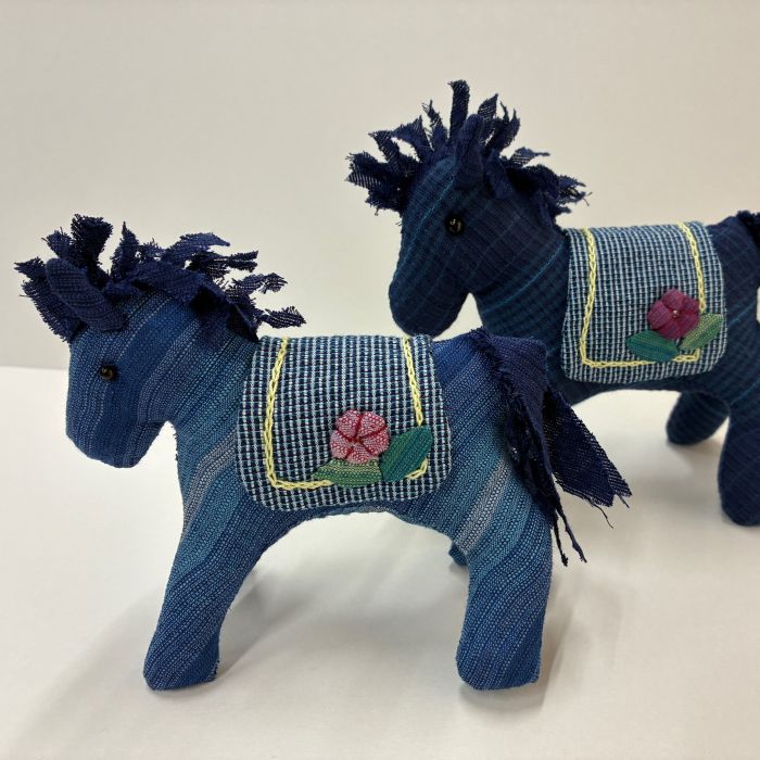 たてがみとしっぽは濃紺のしじら織をカットして作ります。 鞍にはピンクのお花と緑の葉をアップリケして黄色の刺しゅう糸でチェーンステッチをしています。 サイズ：大　高さ9cm×幅12cm、小　高さ7cm×幅9cm キット内容：しじら織、刺繍糸、目玉ボタン、ビーズ 詰め綿は別にご用意ください。