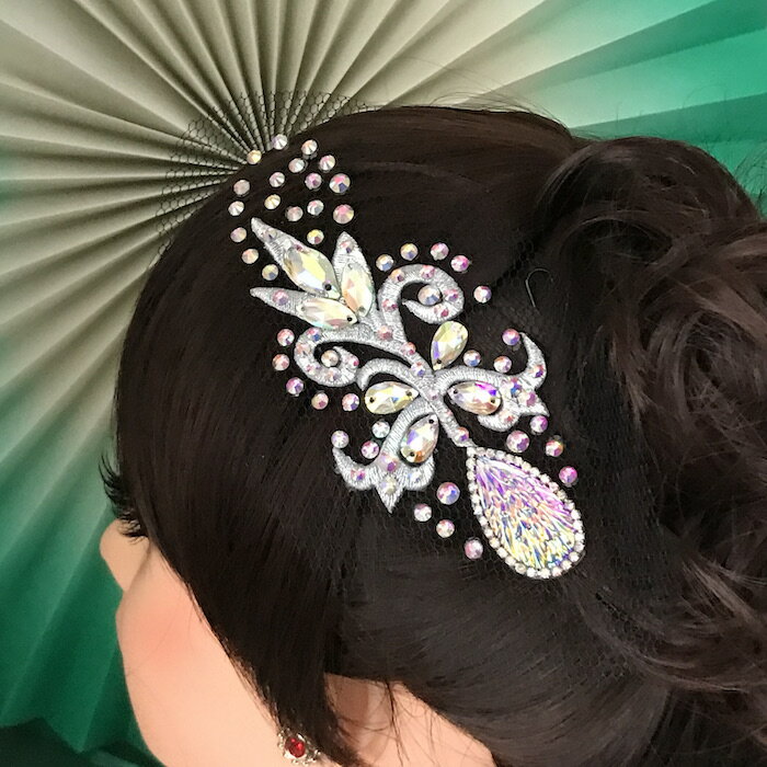 ラインストーン付きのヘアアクセサリーになります。 綺麗なストーンをアクセントとして散りばめ、 様々な色の輝きが放っていますので、 ドレスや衣装などに合わせやすいデザインになっています。 豪華でよく光りますので付けるだけで髪上げが栄えます。 競技会、パーティー、イベント、社交ダンスの衣装にも合います。 取り付けはヘアスタイルをセットした後、 アメピンやUピンで固定してお使いください。 サイズ：H12.5cm W5cm（装飾部分のサイズ） カラー：シルバー・ABオーロラストーン チュール部分は、 ご自身のヘアスタイルやお好みに合わせて カットをしてお使いいただいても大丈夫です。 ※当店オリジナルデザインのハンドメイドです。