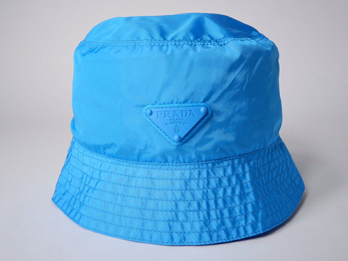アイテム説明 ブランド PRADAプラダ アイテム 2026年 パッカブル Re-Nylon バケットハット2TT338_4ECO_F0GQA サイズ L　頭回り約59cm/ツバ長さ約6cm カラー ライトブルー 素材 リサイクルポリアミド 状態 S:未使用（特記事項:未使用品） コメント 【素材感】→Re-Nylon【商品情報】→このRe-Nylonバケットハットは、プラダの世界を象徴するアクセサリーであり、実用的なミニマリズムと革新を組み合わせたアーバンデザインが特徴です。アクセサリーは軽量バージョンで、特別なポーチに折りたたむことができ、鮮やかな色の独自のパレットで展開されています。トライアングルロゴと同色のディテールが、現代的なアクセントを加えています。 商品番号 MHWA82932 表示番号 DM260721