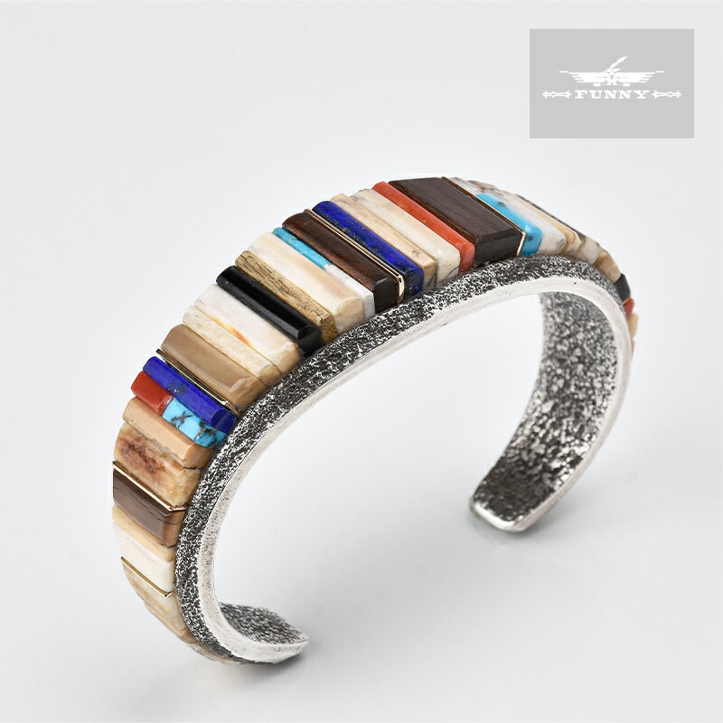 部族NAVAJO（ナバホ） 作者Wes Willie（ウェス・ウィリー） 品名BRACELET（ブレスレット） 素材スターリングシルバーゴールド（14K） 石アイボリーコーラルターコイズラピスラズリジェットアイアンウッド サイズ 最大幅：24mm 最小幅：8mm 内周：135mm 内幅：60mm 開口部：30mm ※インディアンジュエリーにはハンドメイド特有の歪みやずれがあるため、表示サイズには多少の誤差が生じる場合がございます。 ●本製品はハンドメイドによる1点ものです。上記写真の商品そのものを発送致しますが、ご使用のブラウザによっては色の見え方が若干異なる場合が御座いますので予めご了承下さい。 ●本製品は他店舗と在庫を共有しているため、ご注文を頂いた時点では在庫有りと表示されている商品でも、システム上のタイムラグや同一商品への注文集中により、ご注文後に在庫切れとなる場合がございます。ご注文後に在庫切れになった場合はご連絡後キャンセルとさせていただきますので予めご了承下さい。 ●シルバーに細かな傷・擦れが見られますが制作によるものですので予めご了承下さい。 ●石付きの商品に関しましては、本体への衝撃、曲げ歪み、水分を含むことが、石の割れ・欠け・石外れなどの原因になります。デリケートな商品ですのでお取り扱いに十分ご注意下さい。 ●本製品はサイズを縮めたり、広げるなどの負荷をかけますと破損する恐れがございます。ご自身でのサイズ調整は行わないで下さい。ご注文の際は商品スペックをご参照の上、サイズがご不明な場合は当店までお問い合わせ下さい。尚、ご自身でサイズ調整をされ破損した場合の返品・返金及び交換は一切お受けできませんので予めご了承下さい。HIS CREATIVITY DOESN'T KNOW HOW TO STOP TUFA CAST INLAY BRACELET【送料無料】ウェス・ウィリー Wes Willie（ウェス・ウィリー）はナバホ・ネーションで生まれ育ち、溶接工やパイプライン工事などの仕事から金属の扱いを自然に学んでいます。 その後、ナバホのトップ・ジュエラーであるJesse Monongya（ジェシー・モナーギ）氏から、宝石や半輝石、貴金属を扱う本格的なコンテンポラリージュエリー制作の技術を学び、同時に天然素材の組み合わせ方に無限の可能性を見出します。 また、厳選された素材を用いて作品制作を行うことでも有名で、現在では入手困難なハイグレードなターコイズや天然石などを贅沢に使用した美しい作品は、単なるジュエリーの枠を越えたアート作品として高く評価されています。その類稀なる色彩感覚と技術から2017年のサンタフェ・インディアンマーケットにおいては、ジュエリー部門で1位に輝いており、現在最も注目すべきアーティストの一人です。