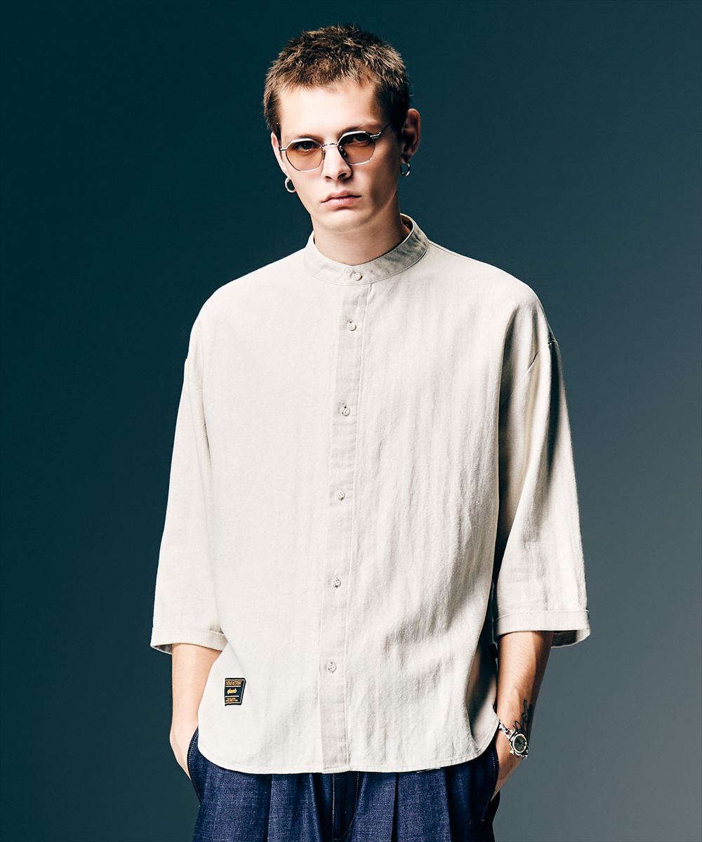 ヴィンテージミリタリーウェアを着想にセレクトしたテキスタイルをミニマルなデザインで提案するStand Collar Shirt。洗練されたスタンドカラーのボディは身幅にゆとりを持たせ、着丈に前後差をつけたオーバーサイズ。ドロップショルダーのアームはレングスを五分袖、袖口をダブル仕様にすることで下側に重心を持たせた変化あるシルエットとなっています。そこに落とし込んだのはシャリ感があり清涼感のある肌触りが魅力となるリネン混ヘリンボーン生地を使用。モックネック調のデザインと相まってリラックスしたアーバンスタイリングを生み出します。 【ご注意】予約商品・お取り寄せ商品（納期10日間以上）のキャンセル、変更はお断りしております。＊クレジット払いの場合、実際の決済はお客様へ商品発送後となります。 素材 サイズ・素材画像参照 サイズ サイズ・素材画像参照 モデル着用サイズ モデル着用サイズ画像参照 ※サイズの測り方は、サイズガイドページを参照ください。 カラー カラー表参照 ご注意 【店舗完売やお取り寄せ不可によるキャンセルについて】このWEBショップで販売中の商品は、実店舗や他WEBショップの在庫数が反映されています。反映にはタイムラグがあるので、在庫変動があった場合、タイミングによってはご用意ができない場合がございます。万が一ご用意ができなかった場合は、メールにてご連絡いたしますので、あらかじめご了承ください。※商品写真はできるだけ現物に近い色に見えるよう撮影いたしておりますが、ユーザー様のモニターやPCの環境により、色の見え方に差異が生じる場合もございますのでご了承くださいませ。