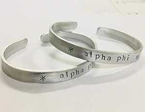 Alpha Phi カフ ブレスレット - 変色しないアルミニウム製のカフに風変わりなフォントでハンドスタンプされており、正式にライセンスされています。 Ann Peden Jewelry Alpha Phi Cuff Bracelet - handstamped in a whimsical font on a non tarnish