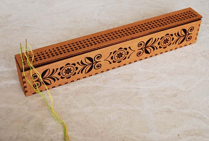 木製ボックスのフタがニードルオーガナイザーになっていて、針を100本刺すことができます。 多色刺しの刺繍に便利です。 それぞれの穴には1～100の数字が振られています。 箱の前面は透かし模様です。 サイズ：28センチ×5センチ×3.2センチ （多少の誤差がございます） 素材：合板 色：ウォルナット ウクライナ製 ※針と糸は商品には含まれません。　