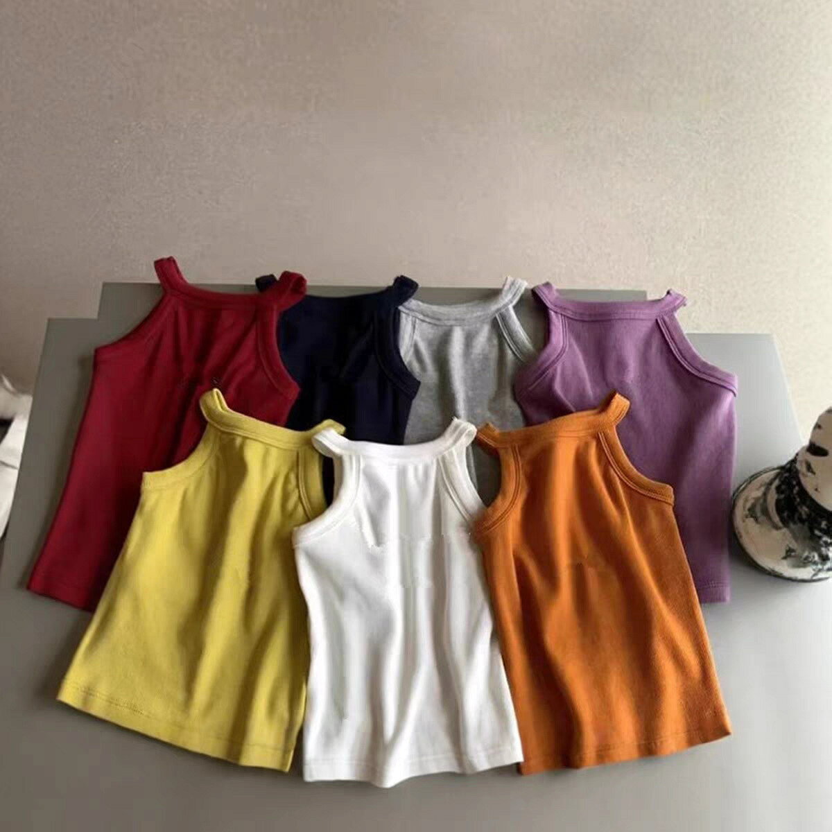 対象年齢：ベビーキッズジュニア（80cm～140cm）性別：男女兼用素材：ポリエステルカラー：レッド / ネイビー / グレー / パープル / イエロー / ホワイト / オレンジ（全 7 色）特徴：無地、太め肩ひも、通気性吸汗性、伸縮性、洗濯耐久性、インナーアウター兼用こちらは、夏のコーデに欠かせない、肌触りの良い無地キッズキャミソールです。7 色の豊富なカラーバリエーションで、どんなボトムスにも合わせやすく、重ね着にも大活躍します。デザインシンプルなホルターネックデザインで、肩ひもが太めでズレにくく、お子様の動きを邪魔しません。無地のシンプルデザインなので、カジュアルコーデからフォーマルな場面まで、幅広く対応できます。インナーとしてもアウターとしても使える、夏の万能アイテムです。