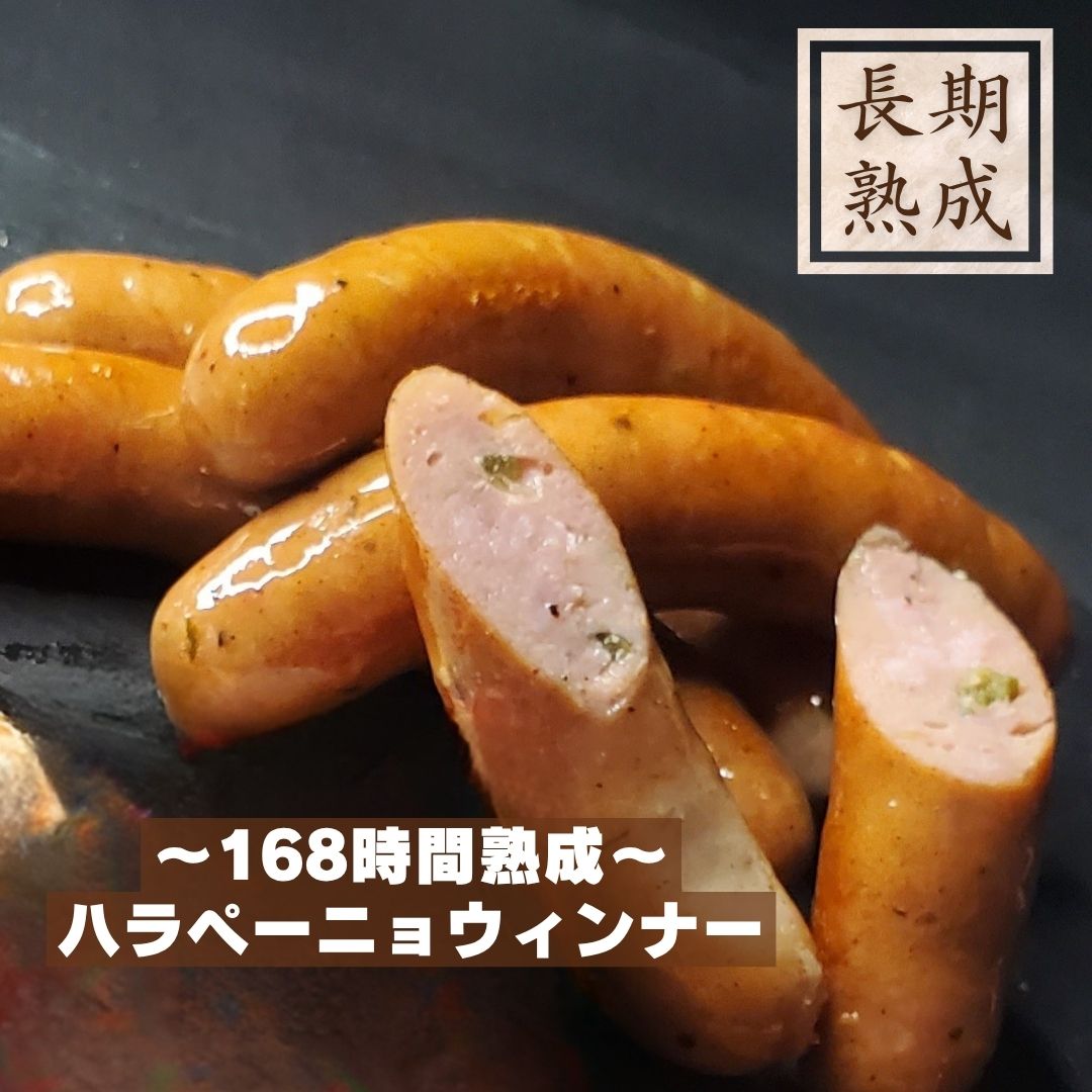 本製品は、以下の添加物を使用しておりません：保存料（ソルビン酸等）、化学調味料（アミノ酸等）、結着剤（リン酸塩等）、増量剤（でんぷん類等） 添加物に頼らないドイツ伝統製法で造り上げたウインナー 辛い物好きにはたまらない！？ 酢漬けのハラペーニョの爽やかな辛味が後をひく、ビールが進むハラペーニョウインナー。 天然腸を使用し、保存料や安定剤などの添加物は使用しない、自然のおいしさ。 熟成肉ウインナーの旨味と、隠し味に入れたブラックペッパーのシャープな辛味が利いたハラペーニョウインナーをご堪能ください。 原材料名：豚肉（国産）、岩塩、三温糖、ハラペーニョ、香辛料／発色剤 (セロリジュース粉末) 内容量：80g 賞味期限：冷凍90日間（-18℃以下で保存) ＊解凍後は冷蔵(10℃以下)で保存し、5日以内にお召し上がりくださいドイツソーセージ職人カール・ブッチングハウス直伝の技を頑なに守る当社の守り続けるドイツ製法の特性は『長期自然漬込み』、『直火式スモーク』といった製造工程にあります。その製法を活かしてハム・ソーセージを造り続ける技術を矢島二郎は当たり前のこととして受け継いでいます。長期自然漬け込み部位ごとにカッティングした肉を塩漬液に2週間程漬込み熟成させます。当社では、漬け込んでいる肉の状態を見ながら重さの違う重石を使い熟成させていきます。じっくり熟成された原料の肉は製品すると約80%?90%のハムになります。この熟成期間を短縮するために、注入器により肉に直接塩漬液（リン酸塩等）を注入したり、結着剤を添加して原料肉の量を増やしてしまう製造方法は、本来の造り方ではありません。そもそも、八郎がハム造りを学んだ大正14年頃には、保存料・着色料・増量剤などは使用していませんでした。 　直火式スモーク2週間程漬け込まれた肉をカッティングし充填し手巻きした熟成肉を燻煙処理します。木が燃えた煙は木の香りが肉に染み込んで、肉の臭みを消す役割があります。それと較べて、オートメーション化されたスモークは煙を循環させているだけですので、煙臭さと色だけがつくだけになります。　　ヘルシーな大発見！豚肉には疲労回復に効果がある『ビタミンB1等、ビタミンB群』が豊富に含まれていることは周知の事実です。もう一つ、とってもヘルシーなことがハムで実証されました。それは、豚肉に含まれているアミノ酸と較べると、ハムに加工された後の”アミノ酸”の含有量は何と2.4倍になるというのです。”アミノ酸”と言えば、人間の体を作る素となるだけでなく、日常生活にも欠かせない成分なのです。また、最近注目のコレステロール低下作用があるペプチドも10％アップするとのことです。その要因は、”漬け込み工程”にあったのです。漬込み液の塩分に肉のタンパク質が溶け出し、そのタンパク質が分解されて、アミノ酸やペプチドが増えていくらしいのです。肉は寝かせて置くだけで酵素の働きによってタンパク質が分解されてアミノ酸やペプチドに分解されます。塩が肉の内部に浸透すると、その作用を促進させるらしいのです。じっくり長期熟成している当社の自然漬込みは、大いにこの効能が活かされていることでしょう。　　素材へのこだわり素材の持つ良さを充分に引き出すために、余計な添加物（保存料や増量剤等）や化学調味料は一切使いません。加わえるのは、塩と砂糖、そして、微量の発色剤だけです。原料の豚肉は、国産豚を中心に、ハムづくりに適した豚肉を厳選しております。