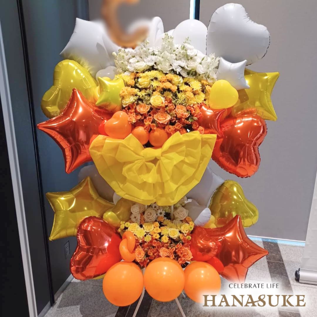 お届け商品 【ショートリボン】【横3色】　バルーンスタンド花2段 お届け日 仕入の関係上、お届けに2〜5日程お日にちを頂く場合がございます。 使用花材 季節の花をメインにおまかせで制作いたします。 サイズ 幅約100cm　x　高さ約180cm　あくまでも目安です。制作内容により異なります。 お届け内容 オアシス入り専用バケツにスタンド台、リボン付き。(リボンの色にご指定がある場合は備考欄へご入力ください。色によってはご対応できない場合もございます。) バケツ部とスタンド台は後日花屋が回収に伺います。 配達エリア 特別対応エリアをご確認ください。但し、注文内容や配達状況によってはお届けが出来ない場合もございます。予めご了承くださいませ。 送料 花助は全国の都市部にある花屋を厳選したフラワーネットワークになります。 都市部であれば送料無料でお届け可能です。 ただ、都市部から離れた郊外へお届けの際は【配送料1,650円（税込）】がかかる場合があります。 ご注文後、配送料については電話もしくはメールにてその旨ご連絡させていただきますのでご安心ください。 無料サービス スタンド花の設置・回収 / 名札 / 配達完了報告 / 画像報告(※画像報告は希望者のみ、配達後5日程度) / 見積書・請求書・領収書 注意 商品ページに掲載されている画像は過去にお届けした一例であり、商品のサンプルではありません。季節・地域によって仕上がりは異なります。予めご了承ください。全国の花贈りに精通したフラワーコンシェルジュが、お客様一人ひとりのご用途に合った、 満足度の高い花屋をその都度厳選し、最高のフラワーギフトを提供します。
