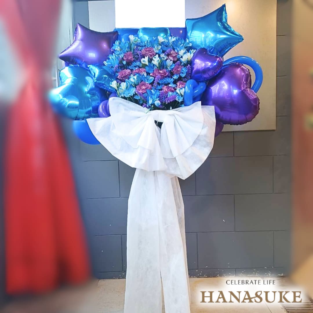 お届け商品 【リボン付き】ドレス・バルーンスタンド花 1段 お届け日 仕入の関係上、お届けに2〜5日程お日にちを頂く場合がございます。 使用花材 季節の花をメインにおまかせで制作いたします。 サイズ 幅約100cm　x　高さ約180cm　あくまでも目安です。制作内容により異なります。 お届け内容 オアシス入り専用バケツにスタンド台、リボン・ドレス付き。(リボンとドレスの色にご指定がある場合は備考欄へご入力ください。色によってはご対応できない場合もございます。) バケツ部とスタンド台は後日花屋が回収に伺います。 配達エリア 特別対応エリアをご確認ください。但し、注文内容や配達状況によってはお届けが出来ない場合もございます。予めご了承くださいませ。 送料 花助は全国の都市部にある花屋を厳選したフラワーネットワークになります。 都市部であれば送料無料でお届け可能です。 ただ、都市部から離れた郊外へお届けの際は【配送料1,650円（税込）】がかかる場合があります。 ご注文後、配送料については電話もしくはメールにてその旨ご連絡させていただきますのでご安心ください。 無料サービス スタンド花の設置・回収 / 名札 / 配達完了報告 / 画像報告(※画像報告は希望者のみ、配達後5日程度) / 見積書・請求書・領収書 注意 商品ページに掲載されている画像は過去にお届けした一例であり、商品のサンプルではありません。季節・地域によって仕上がりは異なります。予めご了承ください。全国の花贈りに精通したフラワーコンシェルジュが、お客様一人ひとりのご用途に合った、 満足度の高い花屋をその都度厳選し、最高のフラワーギフトを提供します。