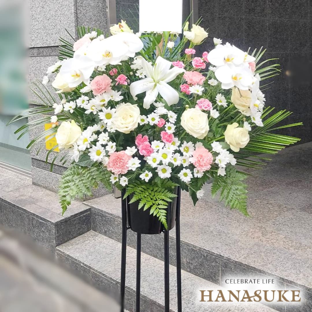 お届け商品 スタンド花 1段 お届け日 仕入れの関係上、1週間ほどお日にちをいただいております。お急ぎの場合は事前にご連絡ください。 使用花材 季節の花をメインにユリを入れておまかせで制作いたします。(ユリの色、本数はおまかせになります。) サイズ 幅約100cm　x　高さ約180cm　あくまでも目安です。制作内容により異なります。 お届け内容 オアシス入り専用バケツにスタンド台付き。バケツ部とスタンド台は後日花屋が回収に伺います。 配送方法 全国の優良花屋から手渡しでお届けします。ただし、当店のネットワーク基準に合った花屋のない地域はお届けできない場合がございます。 送料 花助は全国の都市部にある花屋を厳選したフラワーネットワークになります。 都市部であれば送料無料でお届け可能です。 ただ、都市部から離れた郊外へお届けの際は【配送料1,650円（税込）】がかかる場合があります。 ご注文後、配送料については電話もしくはメールにてその旨ご連絡させていただきますのでご安心ください。 無料サービス スタンド花の設置・回収 / 名札 / 配達完了報告 / 画像報告(※画像報告は希望者のみ、配達後5日程度) / 見積書・請求書・領収書全国の花贈りに精通したフラワーコンシェルジュが、お客様一人ひとりのご用途に合った、 満足度の高い花屋をその都度厳選し、最高のフラワーギフトを提供します。