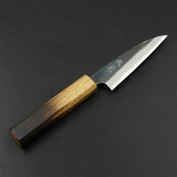 製品仕様 ■サイズ：全長約200mm 刃部 刃渡り約90mm 刃幅約26mm(刃元) 刃厚約3mm 柄部 長さ約100mm 幅約21.5mm(最大) 厚み約16.5mm ■重量：約55g ■材質： 刃部 切刃 青紙スーパー 地金 軟鉄 柄部 炙り白樫(漆塗り) ■刃の形状：両刃 ■刃の仕上げ：黒打ち仕上げ ■柄の形状：八角 ■製造：日本製 ■特徴： 土佐屈指の包丁鍛冶が火造り鍛造したペティナイフです。 切刃に日立安来の最高級鋼である青紙スーパーを使用。 分厚い鋼を叩き伸ばす火造り鍛造により緻密な組織となっています。 更に細心の注意を払って熱処理を行うことで、青紙スーパーの特性を最大限に引き出しています。 柄は、丸太から製材し1〜2年掛けて自然乾燥させた白樫の表面を炙り、白樫の独自の紋様と焦がしの黒のグラデーションが特徴的な八角柄を採用。 仕上げに漆を塗ることで、耐久性と耐薬品性を持つ特徴的な柄に仕上がっています。 小回りがきくため、小さい野菜の皮剥きや、フルーツのカット、飾り切りなどに向いています。 ■切れ味について： 本包丁は鋼製のため、錆防止に刃物用ニスを塗布しているため、箱出しでご使用いただくと本来の切れ味より落ちます。 お使い頂くうちにニスは取れますが、研ぐことで本来の切れ味を体感できます。 また、初期状態では幅広い方に対応できるよう万能な刃付を施しています。 お好みの刃付けがしやすいように仕上げておりますので、 ご自身で研いでいただき、好みの切れ味に仕上げてください。 ■注意： 鍛造から研ぎまでを手造りで行っております。 製造工程上、刃身に傷や酸化被膜の剥がれなどが生じる場合がございます。 そのため、当社では細かい傷や酸化被膜の剥がれなどは、検品の対象外としております。 自由鍛造品ですので商品毎にサイズに差があり、また刃にわずかな歪みや曲りがある場合があります。 食洗機や乾燥機はご使用できません。 ハガネの包丁ですので錆びます。 黒打ち仕上げですので錆びは目立ちにくいですが、こまめに水分を拭き取ってご使用ください。 切刃の青紙スーパーは硬度が高く、一般の包丁より研ぎ難い材質です。 ご理解の上ご購入下さい。 青紙スーパーの包丁を研がれる場合には、下記のシリーズの砥石をおすすめしております。 青紙スーパー推奨砥石はこちら>> 無料ラッピングの詳細はこちら 元兼土佐黒打ち包丁の商品一覧はこちら＞＞高知土佐で屈指の腕を持つ包丁鍛冶が叩き上げた 「ほんまもん」のペティナイフ ねばりのある高硬度の切れ味！ 機械で作られる工場製品と違い、同じ材料・同じ製法を用いても技術の差により大きな違いがでるのが手造り品です。 細心のこころくばりにて丁寧に叩き上げられた形の整った凸凹の少ない刃身と真っ直ぐな美しい刃先の逸品です。 ハガネの最高級品、日立安来青紙鋼をハンマーで幾度も叩き伸ばし鍛造された包丁は不純物が抜け組織が細分化されて、硬く粘り強く鋭い切れ味に仕上がっています。 土佐打刃物400年の歴史が誇る伝統技の結晶 「ほんまもん」の手造り包丁を一度ご使用下さい。 ◆形状・サイズ豊富なラインナップ◆ クルミ柄 出刃包丁 105 150 165 180 210 柳刃包丁 210 240 270 貝裂き 135 和牛刀 180 210 240 小包丁 105 切付型和牛刀 210 240 - 和三徳包丁 170 舟行包丁 150 165 - 土佐型舟行 165 菜切り包丁 青紙1号 青紙スーパー - - - ケヤキ八角柄・青紙1号 和牛刀 180 210 240 - - 切付型和牛刀 210 240 - - - 筋引き包丁 210 240 270 - - 赤紫檀柄・青紙スーパー 和牛刀 210 240 切付型和牛刀 180 210 三徳包丁 170 - 菜切り包丁 165 - 木箱 和牛刀・クルミ柄 210 240 - - 和牛刀・ケヤキ柄 210 240 - - 切付型和牛刀・ケヤキ柄 210 240 - - 和牛刀・赤紫檀柄 210 240 - - 切付型和牛刀・赤紫檀柄 210 - - - 三徳包丁・赤紫檀柄 170 菜切り包丁・赤紫檀柄 165 黒打ちの風合いと土佐400年の伝統技をご覧あれ！
