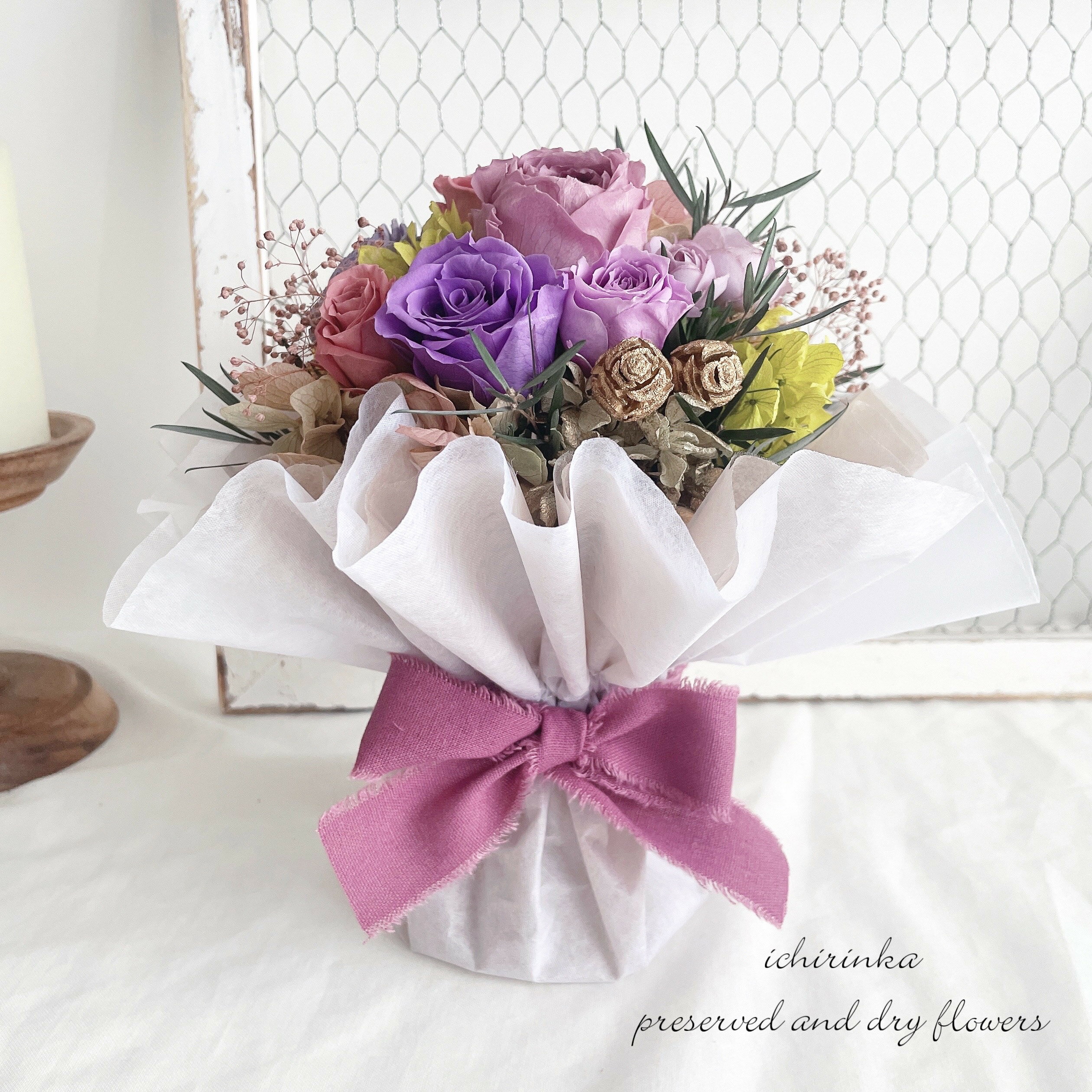 商品情報内容スタンディングブーケ～パープル～（プリザーブドフラワー）ご注文後にひとつひとつ丁寧にお作りする当店オリジナルの商品です説明自立する花束型のアレンジメント。プリザーブドのバラをメインに、上品に仕上げました。古希・喜寿・卒寿のお祝いの品におすすめです！使用花材アーティシャルフラワー・プリザーブドフラワー・ドライフラワーを使用。バラ、紫陽花、ラナンキュラスなど小花などは仕入れ状況により店長おまかせサイズ幅18cm・高さ21cm注意点ブリザードフラワーを使用しておりますので水をあげないでください。直射日光や湿気などで劣化するおそれがありますので、室内でお楽しみください。モニターの発色具合により、実際の色味と異なる場合がございます。メッセージカード【無料】お好きな内容でカードをお作りいたします。オプションから選択または、ご入力ください。無料ラッピングクリアボックスに入れ、リボンをお掛けいたします。無料お渡し用袋マチ付きのビニール製発送目安ご注文日から5日以内に発送いたしますが、お急ぎの場合や希望日に届くかご不安な場合は、ご注文前にお問い合わせいただくことをおすすめします。（即時返答いたします）日時指定も可能です。送料無料 プリザーブドのスタンディングブーケ～ニュアンスパープル～ プリザーブドフラワー アーティシャルフラワー 古希 喜寿 卒寿 花束 ブーケ 紫 バラ フラワーアレンジメント お祝い プロポーズ 結婚祝い 祝電 両親贈呈品 誕生日 長寿祝い 花瓶いらずでそのまま立てて飾れる♪プリザーブドフラワーのスタンディングブーケです。クリアボックス付きで、贈り物にもおすすめです。 きれいが続く...プリザーブドのスタンディング(自立)ブーケ 綺麗が続くプリザーブドフラワーの自立する花束アレンジメント。お祝いに花束を贈りたいけれど、生花だと渡す日が限られてしまったり、遠方への配送に不安を感じている方もいらっしゃるかと思います。事前に準備をしておくことも可能で、枯れたり痛むこともないので遠方への配送もご安心ください。届いてそのまま飾れるので、忙しい方やご高齢の方への贈り物にも大変喜ばれます。古希・喜寿・卒寿のお祝いにもおすすめです！■花材はプリザーブドフラワーを使用■生花に特殊な染料を吸わせることで綺麗な状態を長く楽しむことができるお花です。お水やりなどのお手入れも不要で、花粉飛びもないため老若男女問わず楽しむことができるため、贈り物にも大変喜ばれます。当店では、全て大手業者より仕入れた厳選した花材を使用。自家製の花材は使用しておりません。■プリザーブドフラワーが贈り物に選ばれている理由■●水やりやお手入れ不要でお手軽に楽しめる●花粉飛びもないため安心●届いてすぐに満開のお花が楽しめる●暑い日でもキレイが続き衛生的●生花を加工しているので瑞々しい質感が魅力 いつまでも綺麗が続くプリザーブドフラワーを使用 自立するブーケ型アレンジメント 専用ボックスラッピングで贈り物にもおすすめ 紫を基調としたフラワーアレンジをお探しの方に 古希・喜寿・卒寿のお祝いの品をお探しの方に プリザーブドの花束をお探しの方に 当店の商品は、色や質感、ボリュームなど、厳選した花材を使用し、プロのフローリストがひとつひとつ丁寧に仕立てています。生花のような自然な風合いを残し、ふわふわと優しい色がお部屋をそっと彩ります。配送中に破損がないよう、丁寧に梱包しておりますので遠方の方への大切な贈り物にも安心してご利用くださいませ。 3〜5営業日以内に発送いたします。1