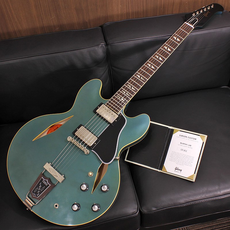 日本限定オーダーのAntique Pelham Blueフィニッシュが最高に格好良い1964 Trini Lopez Standard Reissue！ナローネック仕様になる以前、モデル登場初期をリイシューしたモデルです。これまでも幾度か復刻されておりますが生産数は少なく、日本国内でもレアなモデルの一つと言えるでしょう！〜 Murphy Lab 〜カスタムショップ内に誕生したMurphy Lab（マーフィー・ラボ）は、ナッシュヴィルのギブソン・カスタムショップ内に新設されたラボで、科学的検証に基づく最新の技術を駆使して、ギターのエイジング（ヴィンテージ・ギターの経時変化した外観と弾き心地を再現する処理）を専門に行います。ギブソン・カスタムショップの立ち上げ時のメンバーであり、ヒストリック・コレクション開発のプロジェクト・リーダーとして尽力したトム・マーフィーは、その後新品のギターにヴィンテージのルックスとフィーリングをもたらすエイジングというテクニックで活躍してきました。トムのヴィンテージ・ギターへの情熱と深い知識に裏打ちされた技術によって、ギブソン・ギターの自然なラッカーのクラック、演奏による摩耗を見事に再現しています。トム・マーフィーとギブソンは、経時変化によりウェザーチェックと呼ばれるクラックを生じさせる、1950年代、1960年代のニトロセルロースラッカーを科学的に解析し、その変化のプロセスをひも解き、あらゆるモデルのプロトタイプによるテストを重ねて、ヴィンテージ同様のナチュラル・ウェザーチェックを再現するラッカー・プロセスを開発しました。マーフィー・ラボは、トム・マーフィーがギブソン・カスタムショップのチームを率いて、プロトタイプをもとに、あらゆるボディシェイプ、フィニッシュ、エイジング・レベルの検証を始めたことから、その構想が生まれました。その結果、これまでにないリアリティとこだわりを追求したエイジングを行うために、ギブソン・カスタムショップ内に設立されました。トム・マーフィーの存在と、その芸術的な作品の数々は、ギブソンの歴史の中で重要な役割を果たし、今もそしてこれからもマーフィー・ラボとして永遠に引き継がれていきます。本機は4段階で設けられたエイジングレベルで最もダメージが軽微なコンディションの「Ultra Light Aged」が施された1964 Trini Lopez Standardです。ミュージシャン、俳優としても活躍したTrini Lopez氏の名を冠したTrini Lopez Standardは現代でもDave GrohlやNoel Gallagherといった才能あふれるミュージシャンの使用で知られています。日本限定でオーダーされた本機はまるで本物のようなアンティーク加工が施されたフィニッシュが実に秀逸で、わざとグリーンに焼けた箇所にムラを作ることでリアルさが増しています。Ultra Light Agedは長年ケースに入れて大事に保管されていたかのような、最小限のダメージに抑えられた経年変化の風合いが自然に表現され、穏やかなウェザーチェックや打ち傷等の加工が施されております。指板エッジにはロールド加工が施され、優れたグリップ感がプレイヤーの皆様にはさらに嬉しい仕上げとなっております。ピックアップはUnderwound Custombuckerを搭載。クリスピーでピッキングのニュアンスにレスポンス良く追従する、出力控えめで表現力に優れたトーンが最大の魅力となっております。ルックスのイメージ通りホットなブルーズサウンドや、強めの歪みを掛けても輪郭を失わないためロックバンドのギターヴォーカルの方が歌いながらコードを掻き鳴らすにのにも素晴らしいマッチングを見せてくれるでしょう。トーンを絞った際の音抜け感の良さは勿論のこと、ヴォリュームを絞っても程良くブライトさがキープされるコントローラブルなアッセンブリーは現代的な使用方法とも素晴らしい相性を見せてくれるでしょう！！原点に回帰することでさらなる進化を続けるGibson Custom Shopの最新型の入荷です。Custom Shop製ならではの素晴らしいトーン、Murphy Labが生み出す迫力満点のエイジングをぜひご堪能下さい！Serial No. 122855Weight≒3.85kgブラックハードケース、認定証 付属Body : 3-Ply Maple/Poplar/Maple， Solid Maple Centerblock(w/Window)Neck : Solid MahoganyScale Length: 24.75in / 628.65mmFingerboard Material: Indian Rosewood， Hide Glue FitFingerboard Radius: 12Frets: 22， Authentic Medium-JumboNut Material: NylonNut Width: 1.687in / 42.85mmJoint: Long Tenon， Hide Glue FitBridge: ABR-1 with Nylon SaddleTailpiece: Single Diamond Trapeze with Trini Lopez InsertTuning Machines: Kluson Single Line Strip with Metal ButtonsPickups: Underwound Custombuckerイケベカテゴリ_ギター_エレキギター_Gibson_Custom Shop_新品 JAN:4580568430670 登録日:2023/03/16 エレキギター ギブソン カスタムショップ