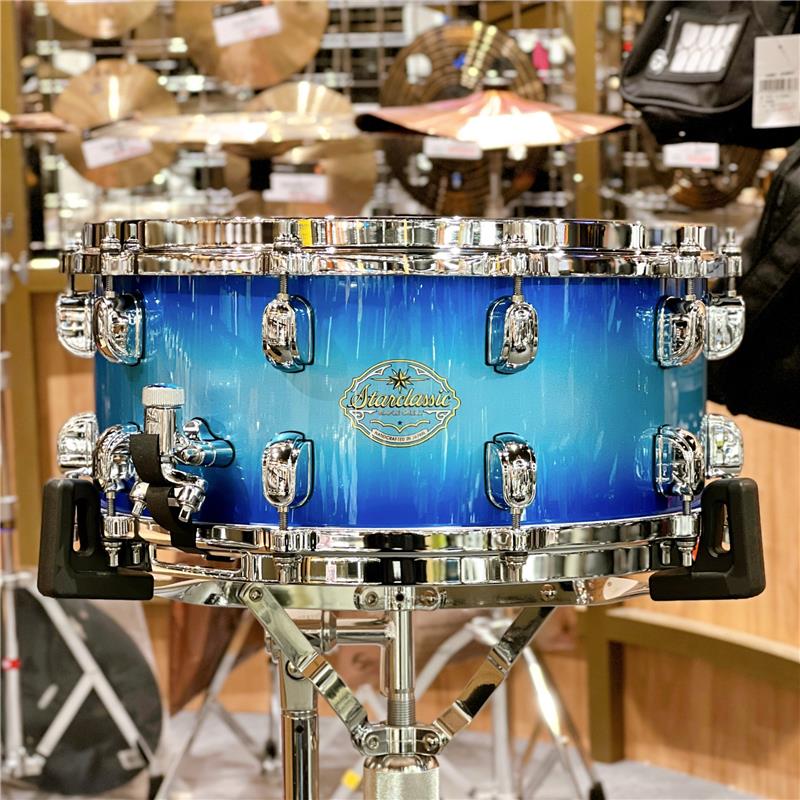 楽器種別：新品TAMA/新品 商品一覧＞＞ドラム【50，000円〜105，000円】 商品一覧＞＞スネアドラム/TAMA 商品一覧＞＞安心してお買い物頂けるよう、スネアもシンバルも丁寧梱包でお届けします！TAMA SMS465T-TWB [Starclassic Maple Snare Drum / 14×6.5][Twilight Blue Burst]【Made in Japan】商品説明※こちら店頭にて試奏を解禁しております個体となりますため、打痕汚れや指紋汚れなどの使用感がございます。何卒ご了承下さいませ。Starclassic Maple Snare Drum約5mmという極薄のメイプルシェルが生み出す、センシティブなレスポンスと明るくオープンなサウンド特性に加えて、剛性の高いダイキャストフープによる明確なアタックを兼ね備えた、オールマイティーな一台です。●Shell（5mm 6ply Maple）センシティブなレスポンスと豊かな「鳴り」を誇る極薄のメイプルシェル。明るくクリアなサウンドはメイプルならではのもの。●Minimum Shell Contactマークは金属バッジではなく、転写エンブレムをシェルの塗装に塗りこめる方式。また、スモールラグ、メイプル材のエアーホール・キャップなど、振動するシェルへの負荷を最小限に抑えたレス・マウント設計です。●Die-Cast Hoops高い剛性を持つ亜鉛ダイキャスト製フープが、ヘッドとフープの接触面を常に垂直に保ちシビアなチューニングにも敏感に対応します。基音のはっきりしたパワーのあるサウンドも大きな魅力。●Linear-Drive Strainerレバーを素早く動かしても、スナッピーがボトムヘッドに当たる接触音を、極限まで減らすことに成功したストレイナー。シェルやストレイナーに余計な負担をかけることなく、スナッピーを確実にヘッドに密着させる構造を採用しています。●Detachable Butt Plateストレイナーバットの2つのボルトを外すことで、スナッピーコードのテンションを保ったままシェルから取り外すことのできるTAMAオリジナル機構。スネアサイドヘッドの交換がより簡単に行えます。●Hold Tight Washerステンレス・ワッシャーとラバー・リングの組み合わせによって演奏中のチューニングの緩みをシャットアウト。ラバー・リングの弾性がショットの衝撃を吸収しフープとテンションボルトが常に密着、シェル振動によるチューニングの狂いを防止します。＜スペック＞サイズ：14×6.5シェル：5mm 6ply Mapleフィニッシュ：Twilight Blue Burst (TWB)フープ：Die-cast Hoop 10-holeラグ / ボルト：MSL-SCT / MS648SHPストレイナー / バット：MLS50A / MLS50Bスナッピー：MS20SN14Sドラムヘッド：EVANS G1 Coated / Resonant 300Made in Japan付属品：ソフトケース、チューニングキーイケベカテゴリ_ドラム_スネアドラム_TAMA_新品 SW_TAMA_新品 JAN:4515276886945 登録日:2026/04/24 スネア スネアドラム タマ 星野楽器