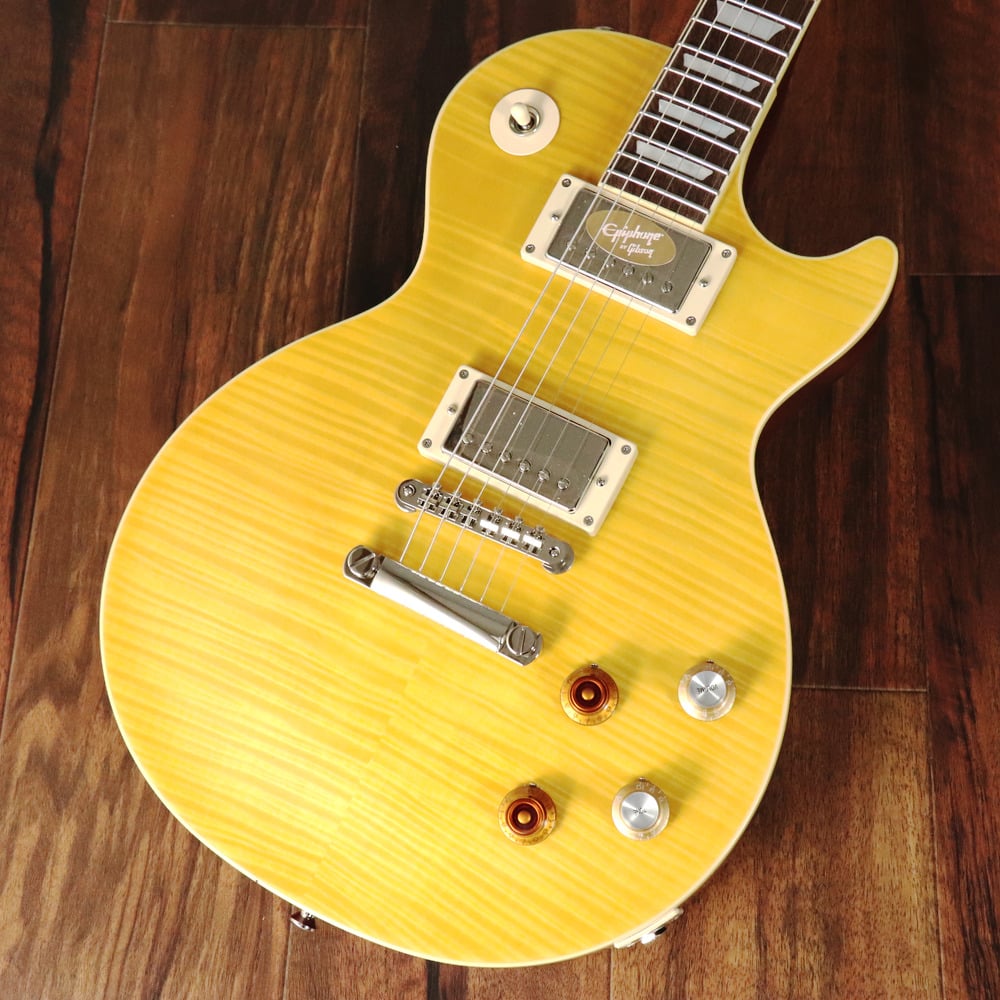 Epiphone Inspired by Gibson Custom Shopから、遂にあの"Greeny"がリリース！ Custom ShopからリリースされたKirk Hammett "Greeny" 1959 Les Paul Standard Murphy Lab Aged、USAからリリースされたKirk Hammett "Greeny" Les Paul Standardが記憶に新しいですが、ついにEpiphone(Inspired by Gibson Custom Shop)ブランドからもあの伝説的なレス・ポールを再現したモデルがリリース！ “Greeny”のストーリーは非常にミステリアスですが、これほどまでに輝かしいストーリーを持つギターはそうありません。 “Greeny”は、これまでに作られたオリジナルのレスポール・スタンダードの中で最も象徴的な1本で、ギターの知名度と並び、実にユニークなサウンドも特徴です。 以前はピーター・グリーン（フリートウッド・マック）が所有しており、その後ゲイリー・ムーアに売却され、シン・リジィとソロ・アーティストとして30年間使用されました。 現在はカーク・ハメットが所有しており、“Greeny”は3人の伝説のギタリストの手に渡り、プレイされ続けているのです。 その特徴的なサウンドとして、ネックピックアップのマグネットを反転させているため、トグル・スイッチをセンター・ポジションにした際に奏でるそのフェイズ・サウンド（逆位相）が挙げられます。 今回リリースされたEpiphone Kirk Hammett "Greeny" 1959 Les Paul Standardは、エピフォンとギブソン・カスタム・ショップの緊密なコラボレーションにより開発されました。 カーク・ハメットが愛用している伝説的なオリジナル"Greeny"にインスパイアされ、オリジナル同様に特徴的なスペックを備えております。 USA製モデルと同じGibson USA Greenybuckerピックアップを搭載し、勿論ネックピックアップは反転されております。 ネックシェイプもCustom Greeny Profileを採用し、さらにリア側のリフレクターノブ、"Spade"ボタンGroverペグなどオリジナルを忠実に再現しております。 そして特筆すべきはヘッドストックシェイプです。遂にEpiphoneのコアモデルでもGibsonオリジナルの“openbook”ヘッドストックを採用されることとなり、Epiphone Kirk Hammett "Greeny" 1959 Les Paul Standardがその最初のモデルとなります。 その他にもGibson Custom Shopとのコラボレーションモデルに相応しく、Switchcraft製ピックアップ・セレクターとアウトプット・ジャック、CTS製ポテンショメーター、Mallory製コンデンサーなど、プレミアムなパーツを採用しています。 ルックスだけでなくサウンド、プレイフィールに於いても、あの伝説的ギター"Greeny"の"魔法"のような魅力を体験することができる、Epiphoneブランド最高峰に位置するモデルです。 EpiphoneとGibson Custom Shopのコラボーレションロゴの入ったヴィンテージスタイルのハードシェル・ケースが付属します。 ■付属品：ハードケース、Epiphoneユーザー登録カード ※ご購入後、同梱されるユーザー登録カードに必要事項をご記入の上、15日以内にギブソン・ジャパンへご郵送ください。ユーザー登録したご本人様に限り、メーカー規定の故障に対して保証が提供されます。 Body Shape | Les Paul Body Material | Mahogany Body Top | Maple with AAA Flame Maple Veneer Neck | One Piece Mahogany Profile | Custom Greeny Profile Nut width | 43mm Fingerboard | Indian Laurel Scale length | 628.65mm Number of frets | 22 Nut | Graph Tech Inlay | Mother of Pearl Trapezoid Bridge | Epiphone ABR Tailpiece | LockTone Stop Bar Tuners | Grover Rotomatic with Kidney Buttons Plating | Nickel Neck pickup | Gibson USA Greenybucker with Reversed Magnetic Polarity;Reverse Mounted Bridge pickup | Gibson USA Greenybucker Controls | 2Volume, 2Tone, 50s Wiring, CTS Potentiomenters, Mallory Capacitors Case | Vintage-style Hardshell with Tan Exterior, Pink Interior, and Custom Artwork ◆重量：3.97kgJAN:4570155996528