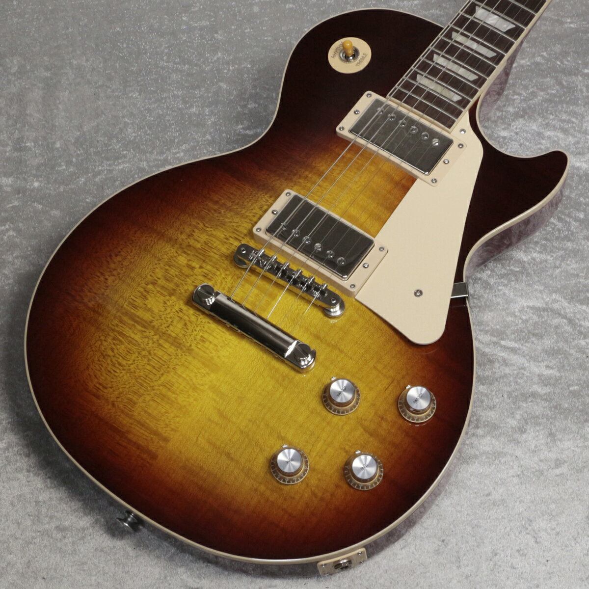 60s Les Paul Standardがパワーアップして登場！ 全世界待望の60s Les Paul Standardがパワーアップして登場！ Gibson 60s Les Paul Standard 、メイプルトップにウエイトリリーフを廃したマホガニーボディ、60年代の薄めのネックを採用した往年のレスポールスタンダードを求めるプレイヤーに最適な一本です。 ピックアップにはアルニコVマグネットを使用したBurstbucker 61R(Neck)/Burstbucker 61T(Bridge)を搭載し、左手の細かなニュアンスやピッキングの強弱、繊細なボリュームコントロールといった演奏表現を余さず出力します。 近年のギブソンに見られる基盤でなく、ハンドワイヤードの電装にはオレンジドロップキャパシターを搭載！ グローバーペグ、ワイヤーなしのABRブリッジにアルミニウム製ブリッジ・テイルピースなど、ヴィンテージを意識した拘りが満載でございます。 使い込むほどに手に馴染み、より一層オールド感が引き立つ至極の一本となるでしょう！ 主な仕様(ネック/ボディ) Neck MaterialMahogany Neck ProfileSlim Taper Scale Length24.75" Fingerboard MaterialRosewood Fingerboard Radius12" Number Of Frets22 FretsMedium Jumbo Nut MaterialGraph Tech Nut Width1.695" End of Board Width2.26" InlaysAcrylic Trapezoids Body MaterialMahogany Body TopAA Figured Maple WeightReliefNone FinishGloss Nitrocellulose Lacquer 主な仕様(パーツ/電装系など) Hardware FinishNickel BridgeABR Tuning MachinesGrover Rotomatics w/ Kidney Buttons PickguardCream Control KnobsGold Top Hats with Silver Reflector & Pointers Switch TipAmber SwitchwasherCream Jack Plate CoverCream Neck PickupBurstbucker 61R Bridge PickupBurstbucker 61T Controls2 Volumes, 2 Tones & Toggle Switch (Hand-wired with Orange Drop Capacitors) Strings.010, .013, .017, .026, .036, .046 CaseHard Shell Case ■ 重量 : 4.02kg ■JAN : 4580228786963 ■付属品：ハードケース、正規保証（要ユーザー登録）