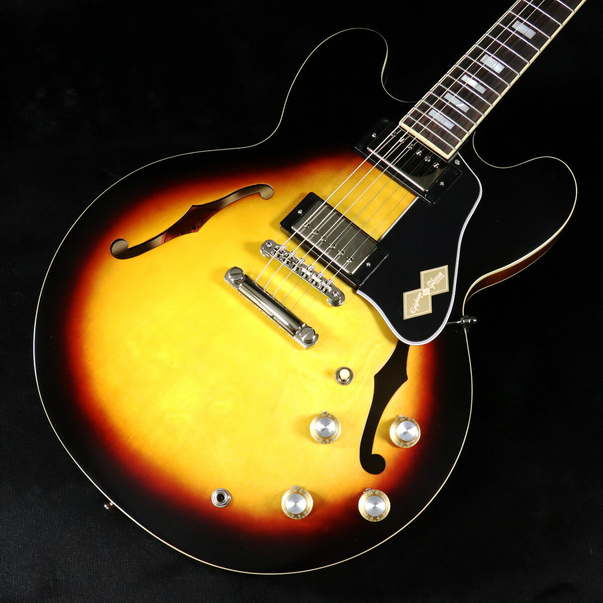 Epiphone Inspired by Gibson Customから新モデルがリリース！1962 ES-335 ReissueGibson ES-335は、ギター史において最も偉大なモデルのひとつです。その卓越した汎用性により、あらゆるジャンルのプレイヤーに愛されてきました。ソリッドボディとシンライン・ホロウボディの特長を融合した構造により高い共鳴性を持ちながらも、内部のソリッド・メイプル・センターブロックによってフル・ホロウボディに比べてフィードバック耐性を高めています。このたび、ギブソン カスタムショップとの緊密な連携により、1962 ES-335 Reissueを発表します。本モデルはGibson CustomのES-335モデルからインスパイアされた一本ですが、Gibson Customが現在復刻していない1962年の仕様を採用しています。丸みのあるカッタウェイ部、スモール・ブロック・インレイ、スリムで弾きやすいネック・プロファイルといった、当時の特徴を忠実に再現しています。本モデルには、5プライのラミネート・メイプル/ポプラ・ボディを採用し、丸みのあるカッタウェイとソリッド・メイプル・センターブロックにより、優れたサステインとフィードバック耐性を実現しています。ワンピース・マホガニー・ネックは薄めの1960sスリムテーパー Cプロファイルを採用し、ローズウッド指板には22本のミディアム・ジャンボ・フレットとマザー・オブ・パールのスモール・ブロック・インレイを装備。さらに、丸みを帯びた指板エッジが心地よい演奏感を提供し、長時間のプレイを快適にします。サイド・ドットのポジションマーカーもヴィンテージの1962 ES-335と同じサイズ・配置を再現しています。ヘッドストックにはGibsonスタイルの“オープンブック”デザインを採用し、EpiphoneロゴとGibsonクラウン・インレイをエイジド・マザー・オブ・パールで装飾。チューナーにはEpiphone Deluxeチューナー（ダブルリング・キーストーン・ボタン付き）を搭載し、Graph Techナットとともにスムーズなチューニングを実現します。ブリッジにはABR-1 Tune-O-Matic、テールピースにはGibsonヒストリック・リイシュー・アルミニウム・ストップ・バーを採用し、ソリッド・メイプル・センターブロックに直接弦振動を伝えることで、優れたサステインを提供します。ピックアップには、USA製Gibson Custombucker humbuckerを2基搭載。CTSポテンショメーターとBlack Beautyペーパーインオイル・キャパシターへのハンドワイヤリング配線により、ES-335ならではの豊かなトーンを実現。ロック、ブルース、ジャズ、カントリーなど、幅広いジャンルに対応します。仕上げには、ヴィンテージの風合いを演出するSixties CherryとVintage Burstの2カラーを用意。外張りがブラックで内張りがゴールドのヴィンテージスタイルのハードケースが付属します。■付属品：ハードケース、ユーザー登録カード※ご購入いただいたご本人様に限り、メーカー規定の故障に対して保証が提供されます。保証修理受付の際は「ご購入時の領収書もしくは納品書」をご提示いただきます。 ■ 重量：3.52kg ■ JAN：4570156008237 ※こちらの商品は現物1点限りを、店頭展示を含め複数のモールに同時掲載しております。 売却に伴う商品情報の削除は迅速を心掛けておりますが、必ずしもリアルタイムではございません。 ご注文後に万一売り切れとなっておりました際は、誠に申し訳ございませんがご容赦くださいませ。 製品仕様 ModelInspired by Gibson Custom 1962 ES-335 Reissue Vintage BurstShapeES-335Body5-ply Layered Maple/PoplarBindingSingle Ply Cream; Top, Back, and FretboardNeckOne Piece MahoganyProfile1960s Slim Taper C-shapeNut width1.69”/43mmFingerboardRosewoodScale length24.75”/628.65mmNumber of frets22NutGraph TechInlayMother-of-Pearl Small BlockBridgeABR-1 Tune-O-MaticTailpieceHistoric Reissue Aluminum Stop BarKnobsGold Top Hat with Silver Reflector with Nickel Dial PointersTunersEpiphone Deluxe, Double Ring Keystone ButtonPlatingNickelNeck pickupGibson CustombuckerBridge pickupGibson CustombuckerControls2Volume, 2Tone; CTS Potentiometers, Black Beauty Paper in Oil CapacitorCaseHardshell with Black Exterior, Goldenrod Interior, and Inspired by Gibson Custom Graphics