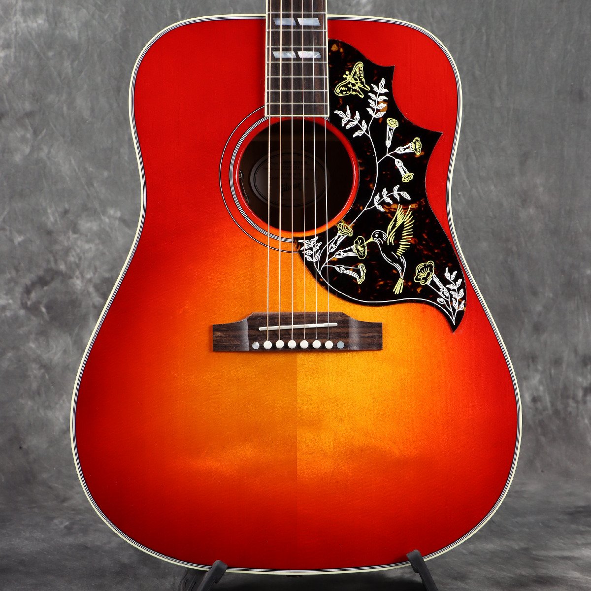 ■こちらの商品は実機画像を掲載しており、店頭未展示の倉庫保管品となります。出荷前に専任スタッフにより楽器の各部機能チェックを行っております。 現行モデル！ギブソン ハミングバードのチェリーサンバーストカラーが復活！ 1960年に誕生した、ギブソン初のスクエアショルダー・ドレッドノート・アコースティックギター「ハミングバード」。 1970年代にはGibsonのラウンドショルダーが全てスクエアショルダーへ移行され、変革期を迎えます。 その布石となったのが、Hummingbirdや1962年に誕生したDoveになります。 もともとHummingbirdは歌の伴奏向けに作られており、通称「ハニートーン」と呼ばれる甘いソフトなサウンドがよく歌に馴染むことで当時フォークシンガーに重宝されるモデルとして君臨していました。 こちらは現行ラインナップのHummingbird Standardで、2024年より待望の復活となったVCS（Vintage Cherry Sunburst）カラーです。 BODYはオール単板で、TOPにシトカ・スプルースを、SIDE/BACKはマホガニーを採用した王道スペック。 TOPにはハチドリが描かれた3ポインテッド・ピックガードを装備しています。 にかわ接着のダブテイルNeckジョイント、スキャロップドXブレーシング、ニトロセルロース・ラッカーフィニッシュ（グロス）はお馴染みの仕様。 PickUpには、L.R.BAGGSのELEMENT VTCをマウントし、サウンドホールエッジ部でVolume/Toneコントロールが可能になっています。 スクエアショルダーならではのボリューム感、倍音成分を多く含んだ優しく広がるサウンドが魅力のハミングバードは、ギブソンアコースティックを代表するモデルの1つです。 ※ラッカー仕上げ特有の塗膜の凹凸や、ヘアラインやバズマークといった研磨痕が生じている場合がございます。いずれもハンドメイドが故のもので、製品・演奏上の問題はございません。予めご了承くださいますようお願い申し上げます。 ■付属品：ハードケース、ストラップピン、クロス、ピックケース、正規保証 ※ご購入いただいたご本人様に限り、メーカー規定の故障に対して保証が提供されます。保証修理受付の際は「ご購入時の領収書もしくは納品書」をご提示いただきます。 ■シリアルナンバー：22405107 ※実物画像を掲載しておりますが、モニター環境によっては若干色合い・明るさが違って見える場合がございます。予めご了承くださいませ。 製品仕様 Body Shape | Hummingbird Body Material | Mahogany Top | Sitka Spruce Back and Side | Mahogany Binding | 5-ply Top, 3-ply Back, Single ply Fingerboard Finish | Gloss Nitrocellulose Neck Material | Mahogany Profile | Round Scale Length | 24.75" Fingerboard Material | Indian Rosewood Fingerboard Radius | 12" Number Of Frets | 20 Frets | Standard Nut Material | TUSQ Nut Width | 1.725" Inlays | Mother of Pearl Parallelograms Joint | Compound Dovetail Neck-to-body Joint; Hot Hide Glue Hardware Finish | Nickel Tuner Plating | Nickel Bridge | Reverse Belly, Rosewood Saddle Material | TUSQ Tuning Machines | Grover Rotomatic Pickguard | .060'' Hummingbird TrussRod | Adjustable Truss Rod Cover | 2-ply Bell, Black and White Bridge Pins | TUSQ Under Saddle Pickup /Preamp| LR Baggs VTC Controls | Soundhole Mounted Volume and Tone