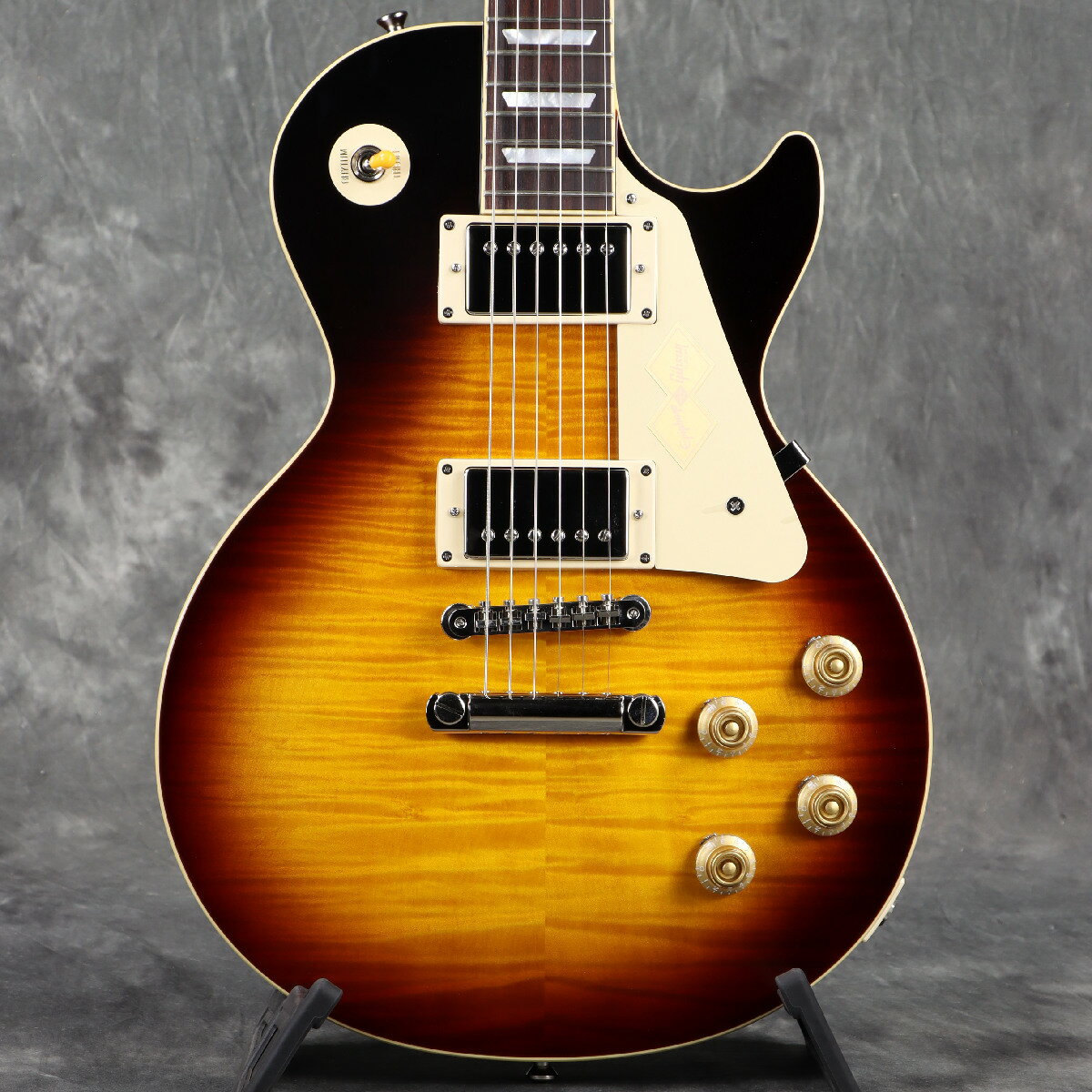 ■こちらの商品は実機画像を掲載しており、店頭未展示の倉庫保管品となります。出荷前に専任スタッフにより楽器の各部機能チェックを行っております。 Epiphone Inspired by Gibson Customから新モデルがリリース！ EpiphoneとGibson Custom Shopのコラボレーションによって製作されるEpiphone Inspired by Gibson Customコレクションは、2024年に大幅に刷新されました。 特に、方方から熱い要望があったにも関わらずなかなか実現することがなかった"Gibsonヘッド"が採用されたことは、多くのGibson/Epiphoneファンにとって非常にエキサイティングなことでした。 そして2025年、Epiphoneのトップラインとして高い評価を得続けているそのEpiphone Inspired by Gibson Customコレクションに、新たなラインアップが加わることとなりました。 多くの方が待ち望んでいたであろうLes Paul Goldtop、Les Paul Special Double Cut、ES-335、SG Standard等、Gibsonギターの歴史を語る上で欠かすことのできないモデル群がリリースされます。 またLes Paul StandardやFirebird I/Vもヒストリックな年式の仕様にちなんだアップデートが施されました。 1959 Les Paul Standard Reissue 1959年製のGibson Les Paul Standardは、世界で最も人気があり、価値の高いヴィンテージ・ギターの一つです。Peter Green、Kirk Hammett、Joe Bonamassaなど、数多くの著名なプレイヤーに愛用されてきました。1960年モデルと仕様は近いものの、1959年ラウンデッド・ミディアムCネック・プロファイルを採用している点が特徴です。1960年モデルのスリムテーパー・ネックよりもやや厚みがあり、多くのプレイヤーに愛され続けています。 このたび、ギブソン カスタムショップとの緊密な連携により、1959 Les Paul Standard Reissueが登場します。貴重な1959年製Les Paul Standardのルックスと演奏性を忠実に再現しながら、手の届きやすい価格を実現したモデルです。 本モデルでは、ワンピース・マホガニー・ネック（ロング・ネック・テノン仕様）を採用し、豊かなサステインを実現。1959年ラウンデッド・ミディアムCネック・プロファイルを採用し、バインディングが施されたローズウッド指板を備えています。さらに、マザー・オブ・パールのトラペゾイド・インレイ、エイジド加工を施したEpiphoneロゴ、シルクスクリーン印刷されたゴールド色の「Les Paul Model」の文字が入ったギブソン・スタイルの“オープンブック”ヘッドストックを採用。サイドドットの位置やサイズも、1959年当時のLes Paul Standardと同じ仕様になっています。ジェニュイン・マホガニー材のボディにメイプル・トップが貼られ、トップには美しいAAAフレイムメイプル化粧板があしらわれています。 エレクトロニクスには、Gibson Custombucker humbucker（USA製、アルニコ3マグネット搭載）を2基搭載し、CTSポテンショメーター、Bumblebeeペーパーインオイル・キャパシター、Switchcraft製トグルスイッチ、1/4インチ・アウトプットジャックを採用。すべてハンドワイヤリングで配線されています。 フィニッシュには、深みのある風合いを演出するヴィンテージ・グロスを採用。ニッケル・ハードウェアとの組み合わせが、美しいヴィンテージの風格を演出します。チューナーには、Epiphone Deluxe “シングルリング” キーストン・ボタン・チューナーを搭載。 外張りがブラウン色で内張りがピンク色のヴィンテージスタイルのハードケースが付属します。 ■付属品：ハードケース、正規保証 ※ご購入いただいたご本人様に限り、メーカー規定の故障に対して保証が提供されます。保証修理受付の際は「ご購入時の領収書もしくは納品書」をご提示いただきます。 ■シリアルナンバー：25021531858 ■重量：4.21kg※実物画像を掲載しておりますが、モニター環境によっては若干色合い・明るさが違って見える場合がございます。予めご了承くださいませ。 製品仕様 Shape|Les Paul| Body|Mahogany| Top|Maple with AAA Flamed Maple Veneer| Binding|Single Ply Cream, Top and Fretboard| Neck|One Piece Mahogany| Profile|1959 Rounded C Medium| Nut width|1.69”/43mm| Fingerboard|Rosewood| Scale length|24.75”/628.65mm| Number of frets|22| Nut|Graph Tech| Inlay|Mother-of-Pearl Trapezoid| Bridge|ABR-1 Tune-O-Matic| Tailpiece|Historical Aluminium Tailpiece| Tuners|Epiphone Deluxe with Single Ring Keystone Button| Plating|Nickel| Neck pickup|Gibson Custombucker| Bridge pickup|Gibson Custombucker| Controls|2 Volume, 2 Tone; CTS Potentiometers, Luxe Bumblebee Paper in Oil Capacitors| Case|Hardshell with Brown Exterior, Pink Interior, and Inspired by Gibson Custom Graphics|