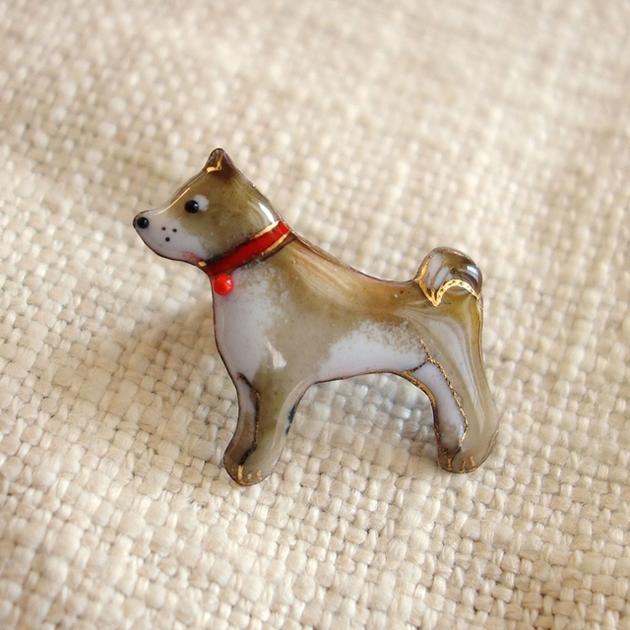 ショップレビューを見る 【UncleZ】七宝焼き　ピンブローチ 柴犬 ＜サイズ＞ 幅30mm×奥行き15mm×高さ30mm 重さ：約6g ＜素材＞銅板・七宝釉薬・ガラス粒子・金液 日本製 手作業で作っている為、同一品番の商品でも、色・柄・サイズ等が微妙に異なりますので、ご了承お願い致します。 伝統工芸風の七宝焼とは、ひと味ちがう、 モダンであたたかみのあるデザインの、アンクル・ゼットの七宝焼のブローチです。 伝統工芸風の七宝焼とは、ひと味ちがう、 モダンであたたかみのあるデザインの、アンクル・ゼットの七宝焼の犬のブローチです。 おすわりしてこっちを見ている姿が愛らしい柴犬のブローチ。 赤い首輪がアクセント♪ ワンちゃん好きの方のプレゼントにもぜひ。 銅板を手で切り出し、叩いて形をつけ、釉薬をのせて炉入れして焼く、 すべての工程を、ベテランスタッフによる手作業でていねいに作り上げました。 そのため、色も表情も、それぞれ微妙に変わります。 ひとつとして同じ物がないのが魅力の、七宝焼のブローチです。 男性ならジャケットの襟に留めたり、ネクタイピンとして。 女性なら、帽子のワンポイントやスカーフ留めに。 寒い時期なら、お手持ちのマフラーやポンチョにも。 また、バッグに着けるのもおすすめ。ひとつだけでも、たくさんでも。 他ではなかなか見られない個性的な見た目で注目まちがいなし？ 金具は真鍮製（主にクロムメッキ）で、しっかりとホールドできるタイプです。 七宝焼（しっぽうやき）とは金属工芸の一種で伝統工芸技法のひとつ。 金、銀、銅、鉄などの金属製の下地の上に釉薬（ゆうやく：クリスタル、鉱物質の微粉末を水とフノリでペースト状にしたもの）を乗せたものを摂氏800度前後の高温で焼成することによって、融けた釉薬によるガラス様あるいはエナメル様の美しい彩色を施すもの。日本国内では、鉄に釉薬を施したものを、主に琺瑯（ほうろう）と呼ぶ。中国では琺瑯（ほうろう／読み：ファーラン）という。英語では、enamel（エナメル）という。 七宝焼きの名称の由来には、宝石を材料にして作られるためという説と、桃山時代前後に法華経の七宝ほどに美しい焼き物であるとしてつけられたという説がある。 中近東で技法が生まれ、シルクロードを通って、中国に伝わり、さらに日本にも伝わった。日本においては明治時代の一時期に爆発的に技術が発展し欧米に盛んに輸出された。（Wikipediaより） その他の七宝焼アクセサリー↑　京の恵み　おすすめ商品ピックアップ　 薩摩つげ櫛 ツイーザー（毛抜き） 木tch：ピアス・イヤリング 七宝焼き・ブローチ ひのきグッズ つげ櫛・櫛ケース 風呂敷 七宝焼・飾り額 木tchブローチ kashin文化足袋 エコバッグ各種 五島産・椿油