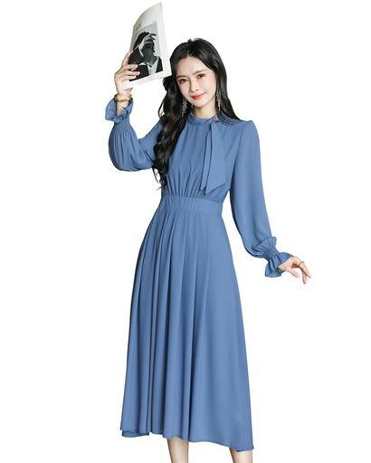 このワンピースは、ドレープ感に優れた高品質な素材を使用しています。肌触りが滑らかで、体に沿って美しく垂れ下がるため、動くたびに流れるようなラインを描き、上品でエレガントな印象を与えます。シワになりにくく、着用シーンを選ばずに美しいシルエットを保てるのが魅力です。 首元はバンドネックデザインで、首元をすっきりと見せるだけでなく、付属のリボンストラップがアクセントにすることができます。襟元にはゴールドカラーの飾りボタンが配置されており、細部までこだわった高級感を演出し、コーディネートの格を上げてくれます。 ウエスト部分はハイウエスト設計になっており、脚長効果を高めると同時に、ギャザーが体を優しく包み込み、くびれを美しく見せます。後ろ側にはウエストベルト が備わっているため、フィット感を調整しやすく、体型に合わせて最適なシルエットを作り出すことができます。 スカート部分にはたっぷりとしたタックが入っているため、気になる下腹やヒップラインを自然にカバーし、美しい A ラインシルエットを作り出します。裾に向かって広がるデザインは、動くたびにふんわりと広がり、優雅な印象を与えます。