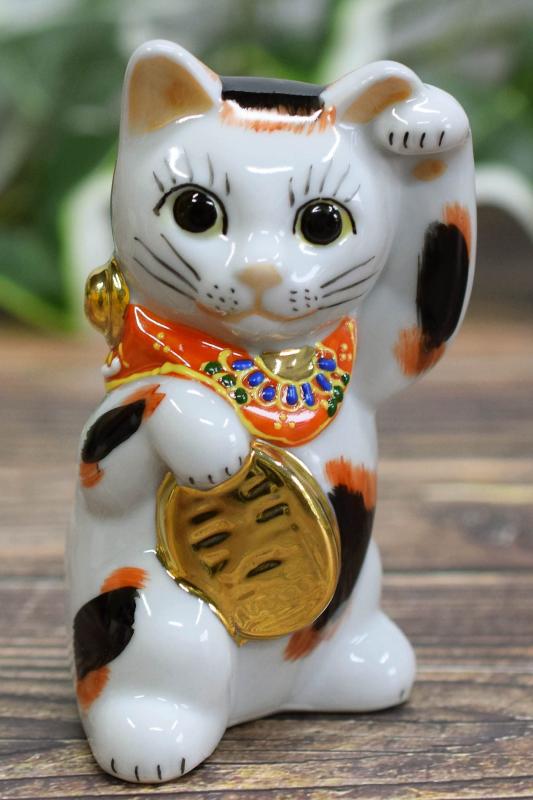 和座の蔵 左手 招き猫 九谷焼 踊る招き猫 三毛 風水 置物 開店祝い プレゼント ギフトサイズ：幅 6cm×奥行 4.8cm×高さ10cm【専用紙箱入り】踊りたくなるほどの福を招くという踊る招き猫ご利益：【右手】金運招福 【左手】千客万来 【白】開運招福 【黒】厄難消除 【赤】無病息災 【金・黄】金運満足 【茶】お悩み解決 【ピンク】恋愛成就九谷焼の技法紹介：盛（Mori）この作品には九谷焼の置物に用いられる特殊技法『盛』が施されています。『盛』とはデコ盛絵具と呼ばれる絵具で「一珍」という独特の道具で描きます。デコ盛絵具は触れるとマッサージ効果ある？と思うくらい凸凹感があります。また『盛』は高度な技術を要し、大変手間の掛かる技法で職人さんも少ないですので、近年では作品自体の希少価値が高くなってきています。贈答用：母の日 父の日 敬老の日 開店祝い 新築祝い プレゼント ギフト などにおすすめ