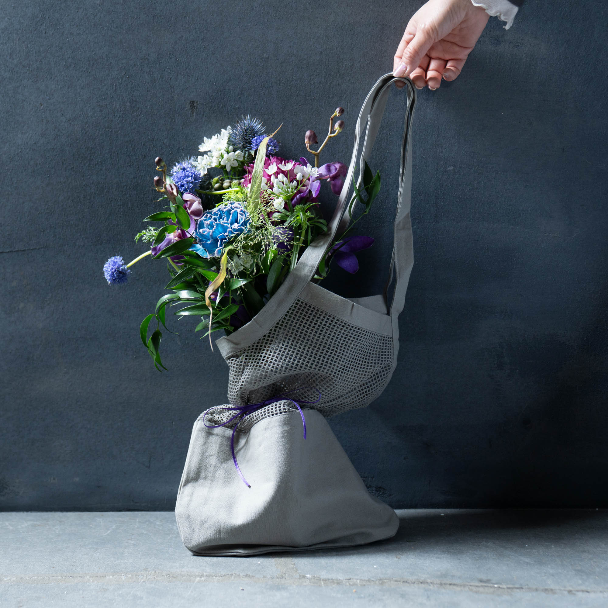 《母の日ギフトにおすすめ》コットンバッグ× 季節のおまかせ生花ブーケSET 生花ブーケとコットンバッグのおしゃれなセット♪ 母の日の贈りものにおすすめしたい、生花のブーケとトートバッグをセットにしました。 季節の花々を束ねたブーケは、フローリストが一点ずつ丁寧に仕立てた特別な仕上がり。 手に取った瞬間にやさしい華やかさが広がり、贈る方の想いをそっと伝えてくれます。 セットのトートバッグは、オーガニックコットン素材のメッシュバッグ。 シンプルながらアクセントの効いた佇まいで、花を持ち帰る時間も印象的なひとときにしてくれます。 普段のお出かけやサブバッグとしても使いやすく、ギフトとしての特別感をさらに高めてくれるアイテムです。 花を贈る喜びと、日常に寄り添う使いやすさをひとつに。 母の日はもちろん、大切な方への感謝を伝える贈りものとしておすすめのセットです。 ＝＝＝＝＝＝＝＝＝＝＝＝＝＝＝＝＝＝＝＝ 〈好評につき延長！超早割りキャンペーン　母の日ギフト10％OFFクーポン配布中〉 正規価格4,950円（税込）⇒ ⇒ ⇒ 早割り価格4,455円（税込） 母の日が近くなると注文が殺到してしまうため、お早めにご注文いただける方向けに早割りキャンペーンをご用意いたしました！ 3月31日(火)までのご注文で、クーポンご利用で特別に10％OFF価格とさせていただきます。 ぜひお早めにご検討ください＊ ※母の日ギフト商品の配送日時につきましては、5月9日(土)もしくは5月10日(日)の配送とさせて頂きます。5月9日(土)・5月10日(日)の日時の指定は出来ませんのでご了承ください。 ※5月9日(土)・5月10日(日)以外の日時をご希望の場合は、備考欄にてお知らせください。 ＝＝＝＝＝＝＝＝＝＝＝＝＝＝＝＝＝＝＝＝ ■母の日ギフト限定オプション 母の日メッセージカード（定型）・簡単なラッピングは無料で承ります。ご希望の方は備考欄よりお知らせください。 自由なメッセカード（250円）をご希望の場合は、オプションからご注文ください。 ■サイズ トートバックのサイズ：高さ63cm・幅30cm 材質 :コットン100%（オーガニック） クリアトートバックタイプもご用意しております。 バッグは、ハンドメイドのため、生産毎にサイズや色の濃淡、材質の風合いに多少の個体差があります。製品の特性としてご理解ください。 ■花につきまして 生花は一つ一つ個体差があり、季節によって入荷出来るお花も異なります。掲載している写真はあくまで一例であり、実際に使用する花材はその都度変わりますので、仕上がりは写真通りではないことをご理解頂ける方のみご購入ください。（花材は当店のおまかせとなります。） ■色味 お花のお色味のご指定がある場合は、備考欄にご記載ください。（ご注文からお届け日までが短期間の場合は、お花の準備が出来ない場合がございますので、お色味のご指定がある場合はお届け日の10日前までにはご注文ください。） ご指定が無い場合は、当店のおまかせとさせて頂きます。 ■配送 ・当店の定休日(火曜日)の兼ね合いで、水曜日着の配送の生花のご注文はお受けできません。なお、生花商品につきましては7〜9月の間は到着時間の指定：不可となります。 ・7月〜9月につきまして、お花の鮮度を保つため生花の商品はクール便での発送とさせていただきます。商品代に通常配送料＋クール便料金（770円）を上乗せした金額でのご提供となりますので、オプションよりご選択ください。何卒ご理解ご了承願います。 また、大阪から配送に2日以上かかる地域へは、生花の配送をお受けできかねますのでご了承ください。（北海道・青森県・岩手県・秋田県・沖縄県、離島など） その他おすすめ商品はこちらから Item Information サイズ トートバックのサイズ：高さ63cm・幅30cm 備考 ・お客様がご使用されているPCや携帯のモニターによって、実物とは見え方が変わる場合がございますのでご了承ください。 ・上記【花につきまして】【色味】【配送】をご確認ください。 ・有料オプションを選択された場合、ご注文完了時には請求金額に反映されません。後ほど注文受付のご連絡を差し上げる際に有料オプションを反映した金額に修正いたします。