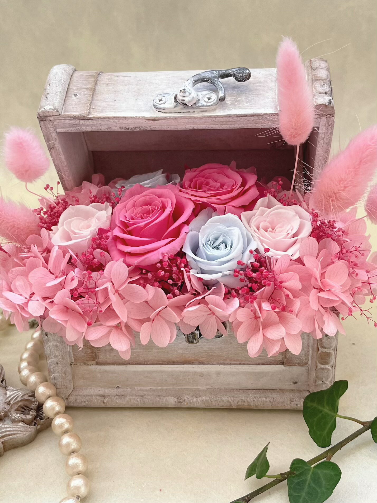 アンティーク調の宝箱にアレンジしました。 華やかなピンクと淡いブルーのバラが、お洒落な雰囲気を演出します。さらに、ピンクのラグラスが可愛らしさをプラス！クリスマスやお誕生日、結婚祝い、母の日、敬老の日など、さまざまなシーンで喜ばれること間違いなしです。大切な人への贈り物にぴったりの一品です。 花材:プリザーブドフラワー(バラ　かすみ草　紫陽花　ラグラス) トランク:木材 サイズ:横12×8 高さ13センチ(ふたを開けた状態) プリザーブドフラワーですので水をかけないで下さい。 撮影用小物は価格に含まれていません。