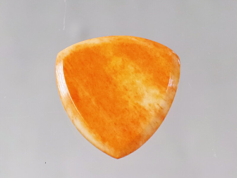 カウボーントライピックシャンファーオレンジスモール Cow Bone Tri Pick Chamfer Orange Small Cow Bone Tri Pick Chamfer Orange Smallは、牛の骨を素材としたトライアングルタイプのピックです。小振りで持ちやすいサイズとなっており、コードよりもリードや速いプレイに向いたスタイルです。 牛骨はギターやベースのナットやアコースティックギターのエンドピンなどに使われる素材で、ギターの弦とも相性がよく、自然な響きを作ります。 このピックは牛骨に着色を行い、独特の風合いに仕上げたピックです。 鮮やかなオレンジ色と、自然素材ならではの風合いが合わさり、1枚1枚違った表情を見せます。遠目にも分かりやすく、ステージなどで落としてもすぐに見つけられます。 弦のすべりは良く、指は滑りにくい、天然素材ならではの特性を持ちます。元々強い素材ですが、トライアングルシェイプとすることで3面を使用でき、さらに長くお使いいただけます。特にこのTri Pick Chamferは、ピックのエッジは丁寧に削られ、弦に引っかかることのない3次元的なシェイプが特徴です。 小振りでスタンダードなトライアングルシェイプ。3.0mm厚でしっかりと物を握っている感覚が心地よいピックです。 ※Wild Picksは自然の素材を用いて手作業で制作しているピックです。 素材の質感を活かし、手作業で制作しているため、1枚1枚、全て外観が違っており、また厚みも若干の誤差がある場合がございます。 "Wild Picks" Animals Pedal Wild Picksは、本来は廃材として処分される自然由来の素材を用い、ハンドメイドで作り出されるピックです。 エコツーリズムな美しいピックは実用性ももちろん、アクセサリーなどの素材としても最適です。 厚みのある硬いピックは、それだけで鋭いアタックと早い音を出します。音が早いと、ピッキングの強弱で音色をダイナミックに操ることができます。一般的な薄くしなるピックよりも重さがあり、また指をピックに安定して固定することができるため、余計な力を必要としません。長いステージでも疲れにくく、自然体でギターをプレイすることができます。これはスタミナだけでなく、よりスムースで良いプレイのためにも大切な要素です。 Wild Picksは自然の素材だからこそ手に馴染み、適度な厚みと重さがあるからこそ強く握る必要もなく、また形状にも工夫することでその厚みを感じないように作られたピックです。　