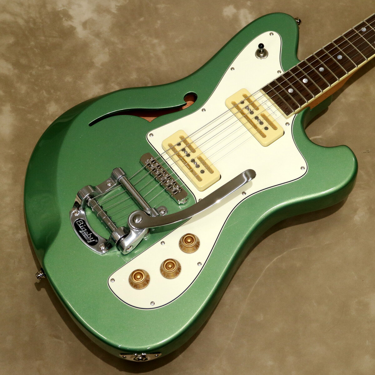 Conquer 59 with Tremoloは、メイプル・トップ&マホガニーを使用したボディーにローステッド・メイプル・ネックを組み合わせ、4点留めのメタル・プレートを用いたボルト-オン・ジョイントで接合しています。 1950～60年代をルーツとした美しい曲線を描いたトラディショナルな上品さと現代的な要素をうまくミックスしたオフセット・シェイプのセミホロー・ボディー・モデルで、ルックス的にも非常にマッチしたビグスビーB50トレモロを搭載したモデルです。 ボディー6弦側にfホールを備えたセミホロー構造のボディーは、エルボー・カットにより演奏性の向上にも一役買っています。 アイボリー・カラーのネック・バインディングが施されたローズウッド・フィンガーボードには、パーロイドのドット・ポジションマークが配置され、25.5インチ(648mm)スケールとなっています。 アルニコ5マグネットを使用したレトロなルックスのJabmasterシングル・コイル・ピックアップを2基マウントしています。 コントロールは、各ピックアップ・ヴォリュームとマスター・トーンで、3ウェイ・トグル・スイッチにてピックアップを切替えます。 ローラー・サドルを装備したバウム・オリジナルLevitatorブリッジを搭載しています。 ネックは手に馴染むシルク・フィニッシュ(艶なし)、ボディーとヘッドはグロス・ラッカー・フィニッシュを採用し、マッチング・ヘッド仕様で、カラーは3プライのホワイト・ピックガードを組み合わせたシルバー・ジェイドです。 ハードケースが付属します。 バウム・ギターズは、30年以上にわたるギター製作に携わってきたMorten Bau(モーテン・バウ)が2015年にBaum Guitarsをデンマークで創設し、スタートしたギター・ブランドです。 当初はルシアー2名でカスタム・ショップとしてスタートし、少量生産を続けていました。 バウム・ギターズの高いデザイン性とコンセプトを受け継いだプロダクション・モデルをアジアのOEM生産にて2021年より開始しています。 アジアのOEM工場で生産したすべての製品をデンマークの本社に在庫し、自社の高い基準にて検品・調整をしたのち、高い品質を保持した製品として世界中に出荷しています。 ブランド名「Baum Guitars」は、創始者のMorten Bauのファースト・ネームの「Bau」にファミリー・ネームの頭文字「M」を合わせたことが由来で、バウムがドイツ語で木を意味することからロゴ・マークには木の葉の意匠が採用されている。 バウム・ギターズは、「Play “Little Vintage, Little Modern” 」の思想を掲げており、ヴィンテージを感じる独自性のある洗練されたモダン・デザインを求めるプレイヤーに向けた製品作りを目指している。 -Specifications- BODY ■Semihollow: Mahogany / Maple top ■Finish: Gloss lacquer ■Thickness: 41mm ■Shape: Conquer NECK ■Headstock: Teardrop &#8210; 3×3 Angle ■Wood: 1 PC Roasted maple ■Profile: C ■Trussrod: Dual-action ■Finish: Silk finish ■Finish Head: Gloss lacquer ■Mount: 4-Bolt on FRETBOARD ■Wood: Rosewood ■Radius: 12” ■Fret Counts: 22 ■Fret Size: Medium Jumbo ■Nut Material: Boneite ■Nut Width: 42.9mm ■Inlay: Pearloid dots ■Binding: Ivory color ■Scale Scale: 25.5″ (648mm) PICKUPS ■Type: Jabmaster ■Shape: P90 ■Magnet: Alnico 5 ■Neck: Output 8.5K ■Bridge: Output 10.5K ELECTRONICS ■Switch: 3 way toggle ■Pots: Alpha 250 k ■Capacitor: 0.047 ■Controls: N/B vol., Master tone HARDWARE ■Tremolo: Bigsby B50 ■Tuners: 23mm head ■Bridge: Baum Levitator ■Finish: Nickel ■Knobs: Gold Bell ■Strings: 10-46 ■Color: Silver Jade ■Case: Hardshell Case ■Weight: 約3.2kg