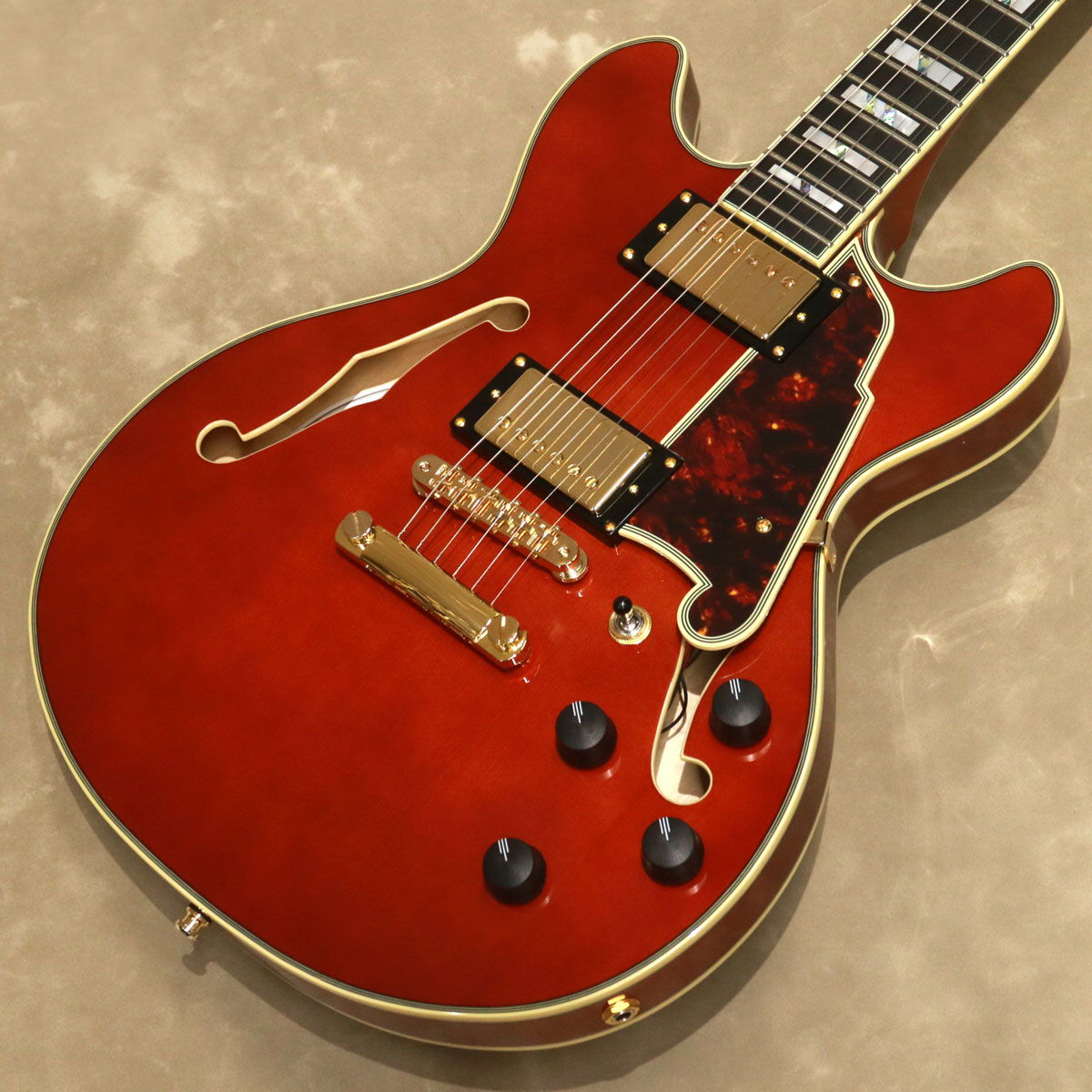 Excel Mini DCは、14インチ幅、1.75インチ厚のオリジナル・ダブル・カッタウェイ・シェイプにセンター・ブロック構造をもったセミホロー・ボディーのモデルです。 ディアンジェリコらしさを感じるオリジナル形状のピックガードは、fホールの一部を思わせるデザインで、5プライのトータス・シェル柄となっています。 ボディー・トップ、ヘッドストックとネックにはバインディングが装飾され、マザー・オブ・パール/アバロンの存在感のあるスプリット・ブロック・ポジションマーカーと組み合わせたデザインはシックでゴージャスな印象を与えます。 ボディーはトップ、サイド&バック共にメイプル、メイプル/ウォールナット/メイプルのネックにはエボニー・フィンガーボードを用いています。 24.75インチのスケールを採用し、ネックはメイプルの間にウォールナットを挟んだ反りや捻じれに強い3ピース構造です。 また、ネック・ジョイントは独自設計の「セット・スルー」ネック・ジョイントとなっています。 さらに、デュアル・アクションのトラスロッドを搭載し、ヘッド側で調整するようになっています。 特徴的なヘッドストック・デザインはディアンジェリコの伝統を継承しています。 トラスロッド・カバーはアルミニウム製で、1930年頃にニューヨークで流行したアール・デコ建築(エンパイア・ステート・ビルディングなど)が建ち並ぶニューヨークの摩天楼にインスパイアされた存在感のあるデザインです。 ピックアップはメタル・カバードのUSAセイモア・ダンカン59ハムバッカーを2基搭載しています。 コントロールは2ヴォリューム、2トーン、3ウェイ・ピックアップ・セレクターのレイアウトで、各ピックアップのトーンはコイル・スプリットのプッシュ・プル・スイッチを兼ねており、トータルで8通りのコイルの組み合わせを備えています。 ハードウェアはゴールドで統一し、チューニングの安定を実現したグローバーのスーパー・ロトマティック・マシンヘッド、チューンOマティック&ストップバー・テイルピースの仕様です。 カラーは、メイプルの木目を生かしたヴィオラです。 ハードケースが付属します。 - Specifications - HEADSTOCK ■D'Angelico Logo: Mother of Pearl D'Angelico New York Logo ■Series Inlay (Front): Mother of Pearl Excel Shield Logo ■Serial Number (Back): Model Name, Serial Number ■Binding: 3-ply, Cream ■Headpin: Cupola ■Tuners: Grover&#174; Super Rotomatic, Gold ■Strings: D'Angelico Electrozinc 10's (10-46) ■Truss Rod Cover: Aluminum Skyscraper, Gold ■Nut Width: 1 11/16” ■Nut Material: Bone FINGERBOARD ■Material: Ebony ■Binding: 3 Ply ■Fretwire: Medium Jumbo ■Scale Length: 24.75" ■Radius: 16" ■Top Inlay: Mother of Pearl/Abalone Split-Block ■Fret Number: 22 NECK ■Material: 3 piece Maple/Walnut/Maple (w/ Single Stripe on the Back) ■Finish: Gloss ■Profile: C-Shape ■Joint Type: Set-Thru ■Truss Rod: Dual Action BODY ■Body Shape: Double cutaway ■Body Style: Semi-hollow (with CB) ■Body Depth: 1.75" ■Body Width: 14" ■Color: Viola ■Finish: Gloss ■Material: Laminated Maple ■Binding: 5 Ply ■Bridge: Gold Tune-O-Matic ■Tail&Tailpiece: Stop-Bar ■Pickguard: Tortoise Scalini (5 ply) ■Pickup Selector: 3-Way Toggle Switch ■Knobs: 4 Ebony ELECTRONICS ■Electronics Overview: 2 Humbuckers/2 volume/2 tone (push/pull)/3-way toggle switch ■Pickup (Neck): USA Seymour Duncan&#174; 59 Humbucker, Gold ■Pickup (Bridge): USA Seymour Duncan&#174; 59 Humbucker, Gold ■Pots: 500k ■Output Jack: Standard mono HARDWARE ■Hardware Color: Gold ■Case: Deluxe Hardshell ■Weight: 約3.1kg