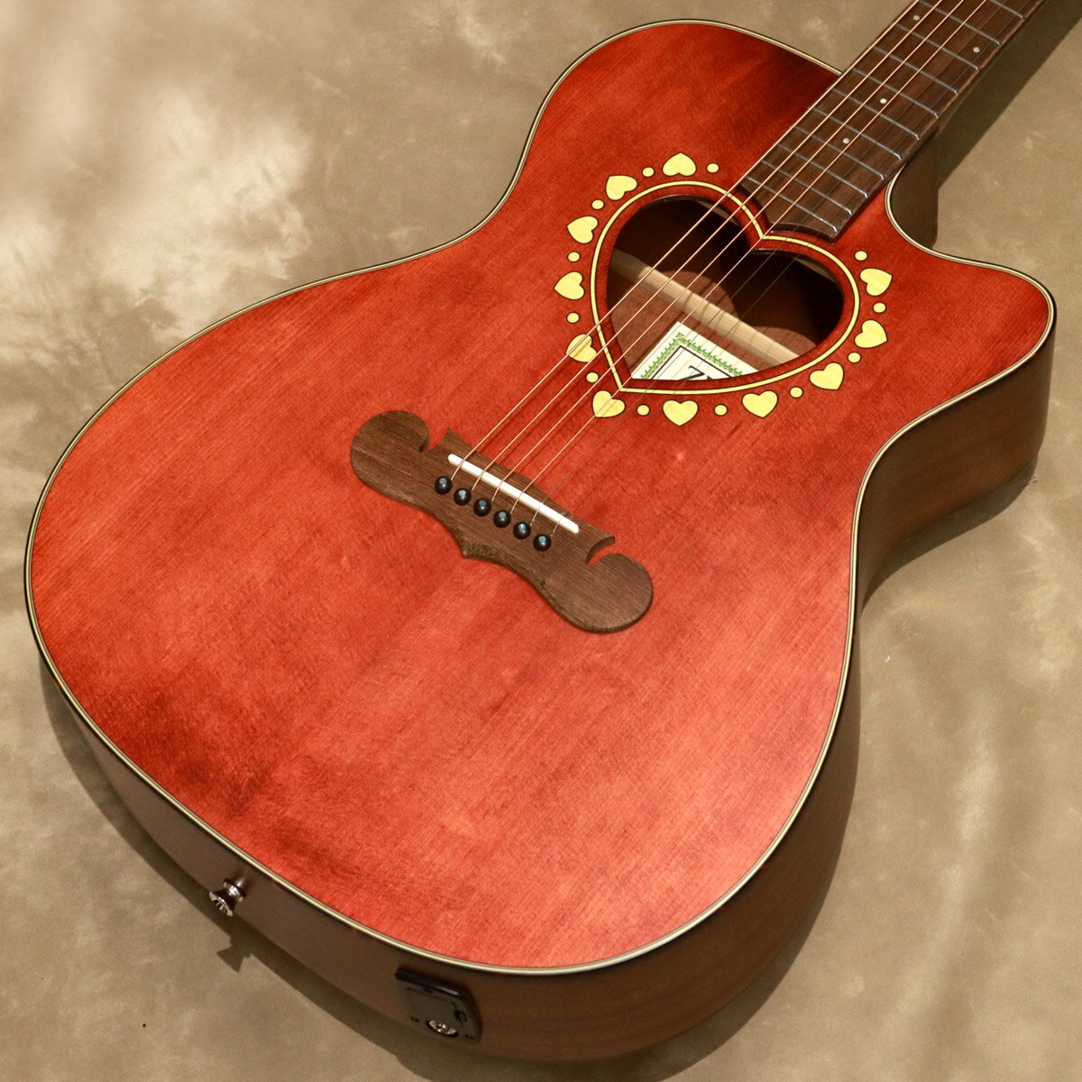 ※画像はサンプル画像になります。 ゼマイティス・アコースティックにアンダーサドル・ピックアップ搭載のエレクトリック・アコースティック・モデルCAF-85HCW。 CAF-85HCWは、人気のハート・サウンドホールのオーケストラ・カッタウェイ・モデルであるCAF-80HCWを基に、ローズウッド柄やメイプル柄のウッディーなロゼッタを採用したモデルです。 マザー・オブ・パールのダイヤモンド・インレイが輝く特徴的なヘッドストックを持ったネックはマホガニー、フィンガーボードにはローレルを採用し、20フレット仕様の14フレット・ジョイントとなっています。 ゼマイティスの伝統的なハート型のサウンドホールの周りに特徴的なハートをちりばめたデザインとマスターシュ・ブリッジのオリジナル・デザインは非常に魅力的です。 トップ・ブレイシングは、サウンドホールの形状やボディーのサイズを考慮して、最大限の鳴りを引き出すためにフォワードXブレイシングを採用しています。 また、板材の時に真空状態で熱を加えることで余分な水分やミネラルを取り除いたソリッド・スプルースをボディ・トップに使用している点が特長で、サイドとバックにはサペリを採用し、狂いの出にくい安定したボディ剛性を実現しました。 湿度や気温などの外部要因でサウンドが変化しやすいアコースティック・ギターにとって大きなアドバンテージです。 ボディー・サイドには4バンドEQとクロマティック・チューナー機能を持ったプリアンプを搭載し、お好みのトーンでアンプなどの外部機器にも出力できます。 木地着色を行うことで木目を消すことなく素朴な仕上がりを目指したアンティーク・フィニッシュのフェイデッド・レッドのトップ・カラーで、年齢や性別を問わず長年親しんでいただけます。 主な特徴 ●アンダーサドル・ピエゾ・ピックアップからのサウンドをコントロールするプリアンプ・システム。コントロールはVolume、Treble、Middle、Bass、Presence。便利なチューナー機能も装備。9Vバッテリーを使用。 ●サウンドに広がりを与えるハート形状のサウンドホールと、ハートとドットが交互にちりばめられたロゼッタ。 ●その形状から、英語で口ひげを意味する「マスターシュ」と命名されたブリッジ。 ●付属ギグバッグは、大きな前面ポケット付き。ダブル・ショルダー・ストラップでバックパック・スタイルでの運搬が可能。 - Specifications - ■Top: Solid Spruce ■Back & Sides: Laminated Sapele ■Bracing: Forward X ■Neck: Mahogany ■Nut Width: 43mm ■Fingerboard & Bridge: Indian Laurel ■Fretboard Radius: 400mm ■Nut & Saddle: Bone ■Scale Length: 630mm ■Frets: 20 ■Finish: Satin Urethane ■Body Length: 490mm ■Body Width (Upper Bout): 282mm ■Body Width (LowerBout): 392mm ■Body Depth (Upper): 96mm ■Body Depth (Lower): 108mm ■Preamp: EX-4 with Zemaitis Logo ■Strings: .012 / .016 / .024 / .032 / .042 / .053 ■Weight: 約2.1kg ■Case : Gigbag