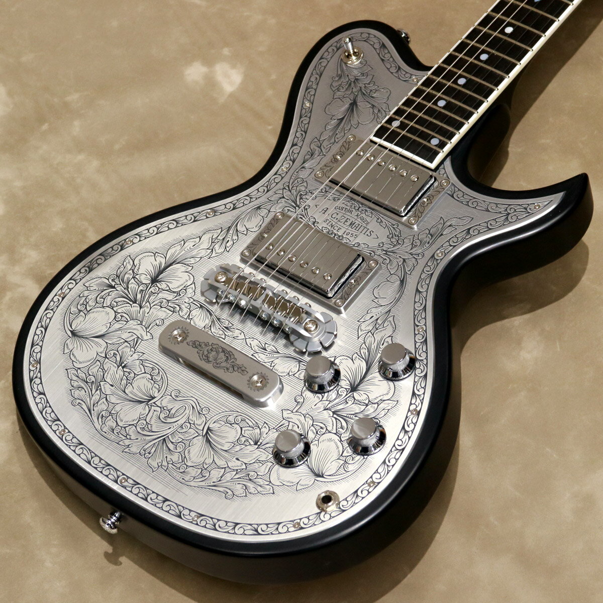 ゼマイティスより、トップに彫金装飾を用いたメタル・フロント・モデル「MFG-AC-24 DUO」が登場しました。 ゼマイティス最高級モデルの生産工場と同じ工場で製作した、ハイグレードなモデルです。 MFG-AC-24 DUOは、デュオ・カッタウェイのボディー・スタイルで、ボディーとネックに厳選されたアフリカン・マホガニー、フィンガーボードはエボニーを使用しています。 635mmのスケールで、セット・ネック・ジョイント、ミディアム・サイズの24フレット仕様です。 ボディー・トップのアルミ合金のプレートにゼマイティスらしいリーフ柄の彫金装飾を全面に加え、伝統を示す「A.C.ZEMAITIS SINCE 1955」の文字が刻まれたデザインなどクラシックなルックスが特徴です。 ゼマイティス・オリジナルのアルミ合金を使用したブリッジ＆テイルピースを搭載し、ゼマイティス独自のトーンを生み出す要素となっています。 同様にアルミ合金を用いたヘッドのダイアモンド・エンブレム、トラスロッド・カバー、テイルピースやピックアップ・リングをはじめ、アウトプット・ジャック・プレート、コントロール&スイッチ・バック・プレートに至るまで彫金を施しています。 ピックアップは、メタル・カバード・タイプのDragon Classicハムバッカーを2基搭載、コントロールは定評のあるCTSポットを使用し、各ピックアップ・ヴォリュームと各ピックアップ・トーンのレイアウトです。 スイッチクラフト製の3ウェイ・ピックアップ・セレクター・スイッチを備え、トーンのキャパシターはオレンジ・ドロップを使用しています。 さらに信頼性の高いゴトー製のチューナーを使用しています。 フィニッシュはラッカーを使用し、カラーはブラックです。 ハードケースが付属します。 Made in Japan ●2つのピックアップの間には、「A.C.ZEMAITIS SINCE 1955」の文字が彫金されている。 ピックアップ・リングは、最新の弦の角度にあわせたアングル付きではなく、あえて従来のフラット・タイプを合わせることでクラシックな印象を持たせている。 ●トップのメタルプレートはゼマイティスの伝統であるリーフ柄の彫金デザイン。 -Specifications- ■Body : African Mahogany ■Body Top : Flat Shape ■Neck : 1Piece African Mahogany ■Neck Binding : WH ■Neck Finish : lacquer ■Neck Joint : Set Neck ■Finger-board : Ebony / 305R ■Nut : Bone 43mm ■Scale : 635mm ■Frets : 24 Medium ■Pickups Neck : Dragon Classic N ■Pickups Bridge : Dragon Classic B ■Controls : 2 x Volume, 2 x Tone , 3Way Pickup Toggle Switch ■Bridge : ZBR-2 ■Tailpiece : ZTP-1 ■Machine Head : Gotoh&#174; SG301-01 Chrom ■Potentiometers : CTS&#174; A 500KΩ ■Capacitors : Orange Drop&#174; (0.022μF) ■Selector Switch : Switchcraft&#174; (SC-1212DX) ■Output Jack : Switchcraft&#174; SC11MONO ■String Gauge : 010, 013, 017, 026, 036, 046 ■Body Finish : Lacquer ■Colors : Black ■Case : Hardcase ■Weight: 約3.95kg