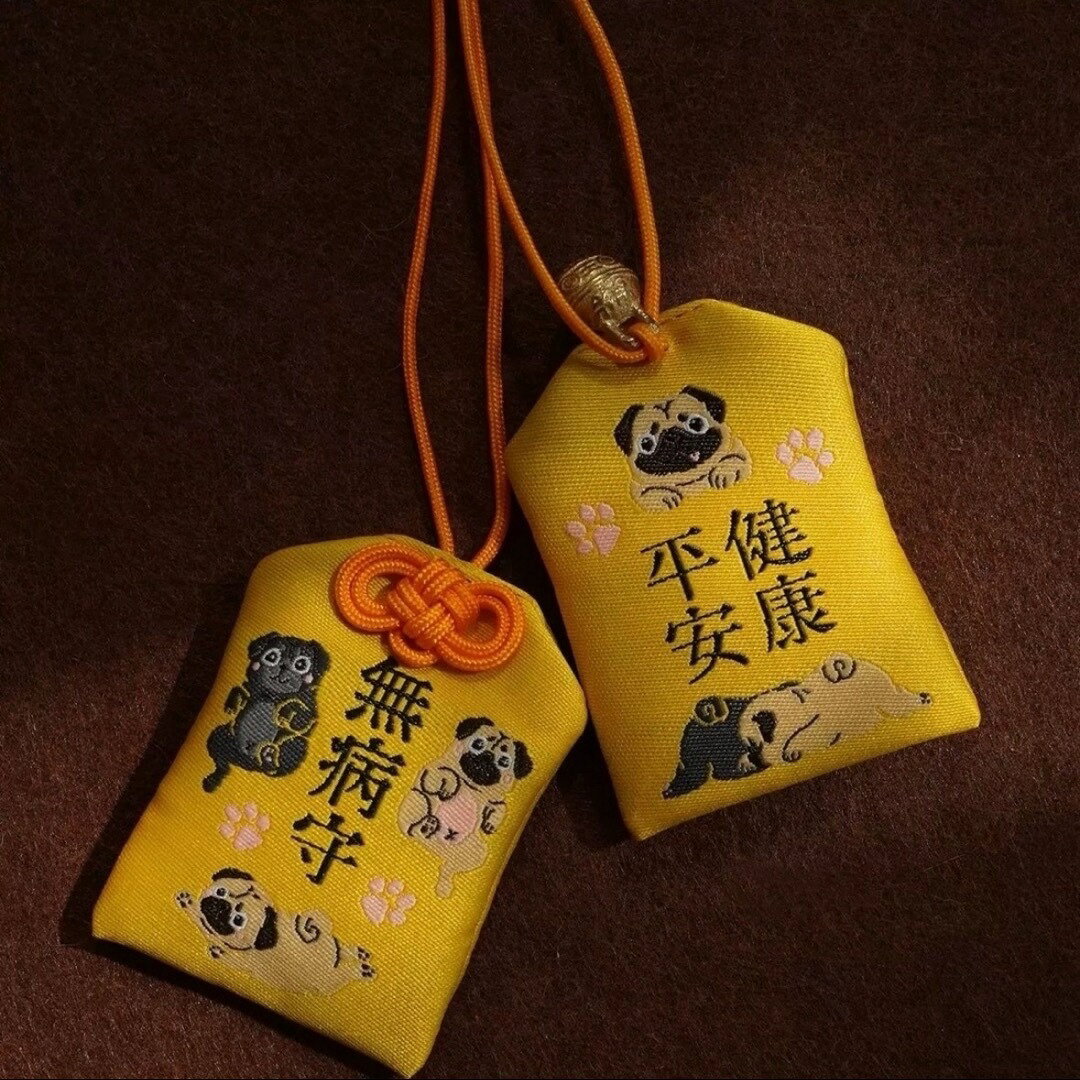 商品説明 パグ好きさんにぴったりな、表と裏に可愛いパグの刺繍が施された両面デザインのお守りです。1つのお守りで、「無病守」と「平健安康」ふたつの願いを込めることができます。■&nbsp;表面：「無病守」黒パグ・フォーンパグなど、3匹の元気なパグたちがデザインされています。病気知らずで健康に過ごせますように、という願いが込められています。■&nbsp;裏面：「平健安康」くつろぐ姿が愛らしい2匹のパグが描かれており、穏やかで健やかな毎日を祈願したデザインです。上部には小さな鈴付きで、揺れるたびに癒される優しい音色もポイントです。愛犬のお守りとしてはもちろん、犬好きな方へのプレゼントやお出かけバッグのアクセントにもぴったりです。【サイズ】約7cm&nbsp;×&nbsp;約4.5cm【素材】ポリエステル（高品質刺繍仕上げ）※本商品は宗教的な意味合いではなく、雑貨・インテリアアイテムとしてお楽しみください。