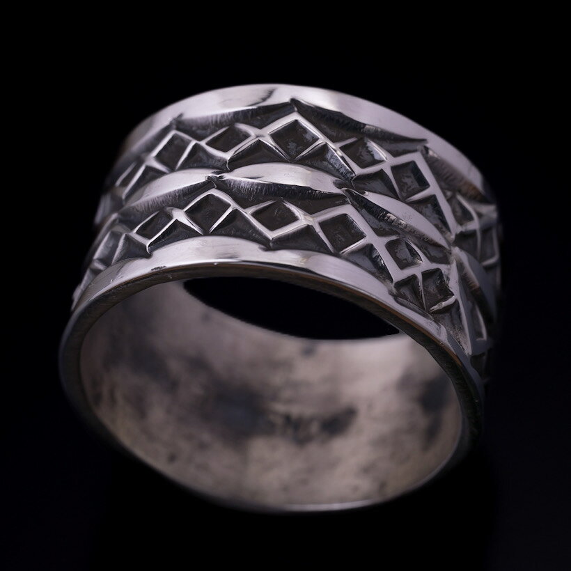 部族Navajo/ナバホ刻印ありサイズ ◎号数：22号 ◎縦幅：約12mm ◎厚み：約1.3mm ◎重量：約8g 【送料無料】備考・ラッピングサービスを承っております。お客様の大切な贈り物を心を込めてラッピングさせていただきますので、どうぞご利用くださいませ。 ・商品は実在店舗での販売もしておりますのでタイムラグにより在庫数のずれが 生じる場合がございます。在庫ありの表示でも品切れの場合がございますので、予めごご理解の上ご注文くださいますようよろしくお願いいたします。 ・撮影時の照明等の影響やPCディスプレイの特性の差などで、実物とは色合いが異なって見える場合がありますので、予めご了承下さいますようお願い致します。 ・本製品はアーティストによる手作業で一点一点作られているため、スタンプの配置や細かな仕上がりにわずかな個体差がございます。ハンドメイドならではの、世界に一つだけの風合いとしてお楽しみください。ナバホ族 Sunshine Reeves 1/2" クラシックスタイル リング 22号Navajo/ナバホ族のアーティスト Sunshine Reeves/サンシャイン・リーブス氏に制作を依頼したバンドリングです。代々受け継がれてきた伝統的なナバホスタイルでありながら、現代のファッションにも不思議と馴染む、圧倒的な完成度を誇る作品に仕上がりました。存在感のある11mmのリング幅に、隙間なくびっしりと施されたスタンプワーク。これぞサンシャイン・リーブス氏の真骨頂です。一打ち一打ち、寸分の狂いもなく刻まれた幾何学模様は、伝統的なインディアンジュエリーの力強さと、工芸品のような美しさを兼ね備えています。しっかりとした幅感と厚みがあるため、手元が寂しくならず、これ一つでスタイリングの主役になってくれます。主役級の存在感を放ちながらも、ベースはシンプルなバンド（平打ち）リングなので、アメカジから綺麗めなスタイルまでどんなコーディネートにも馴染む抜群の器用さを持っています。実際に指に通してみると、その見た目のボリュームからは想像できないほど、驚くほどしっくりと馴染みます。指への収まり（フィット感）が非常に良いため、「普段あまり太めのリングを着けない」「インディアンジュエリーは初めて」という方でも違和感なく、自然に日常使いしていただけます。使い込むほどに深い味わいへと変化していくのがスターリングシルバーの醍醐味です。日常使いでガシガシ着用することで、スタンプワークの凹凸に陰影が生まれ、さらに立体感と渋みが増していきます。あなただけの特別なエイジングをぜひお楽しみください。