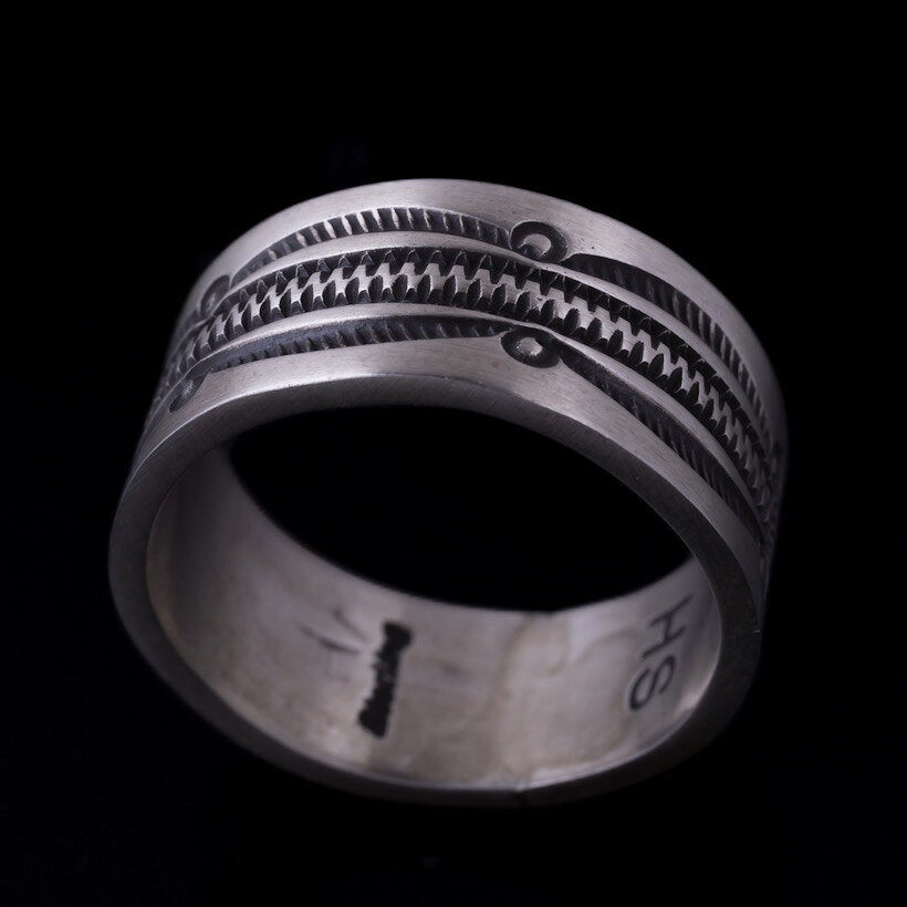 部族Navajo/ナバホ刻印ありサイズ ◎号数：23.5号 ◎縦幅：約10mm ◎厚み：約1.5mm ◎重量：約10g 【送料無料】備考・ラッピングサービスを承っております。お客様の大切な贈り物を心を込めてラッピングさせていただきますので、どうぞご利用くださいませ。 ・商品は実在店舗での販売もしておりますのでタイムラグにより在庫数のずれが 生じる場合がございます。在庫ありの表示でも品切れの場合がございますので、予めごご理解の上ご注文くださいますようよろしくお願いいたします。 ・撮影時の照明等の影響やPCディスプレイの特性の差などで、実物とは色合いが異なって見える場合がありますので、予めご了承下さいますようお願い致します。 ・本製品はアーティストによる手作業で一点一点作られているため、スタンプの配置や細かな仕上がりにわずかな個体差がございます。ハンドメイドならではの、世界に一つだけの風合いとしてお楽しみください。 ・石付きの商品は、曲げたり歪ませたりすることや、水分が付着・浸透することにより、石の割れ・欠け・外れなどが生じる場合がございます。デリケートな商品ですので、お取り扱いの際は十分ご注意ください。ナバホ族 Herman Smith 3/8" クラシックスタイル リング 23.5号Navajo/ナバホ族のアーティスト、Herman Smith/ハーマン・スミス氏に制作を依頼したバンドリングです。ナバホ族に古くから受け継がれてきた伝統的なデザインをベースに、現代のファッションにも自然と馴染む一品に仕上げられています。約10mmのしっかりとしたリング幅に、細かな幾何学模様のスタンプワークを施しています。一打ち一打ち丁寧に刻み込まれた凹凸が、ナバホジュエリーならではの力強さと、ハンドメイドならではの温もりを際立たせています。程よい幅と厚みがあり、これひとつでも手元に十分な存在感を与えてくれるのも魅力。存在感のあるボリュームながら、シンプルな平打ちのバンドリングなので、アメカジからきれいめなスタイルまで幅広く合わせていただけます。見た目のボリューム感に対して指馴染みも良く、日常使いしやすい仕上がり。伝統的なナバホスタイルと、Herman Smith氏ならではの丁寧なスタンプワークをぜひお楽しみください。