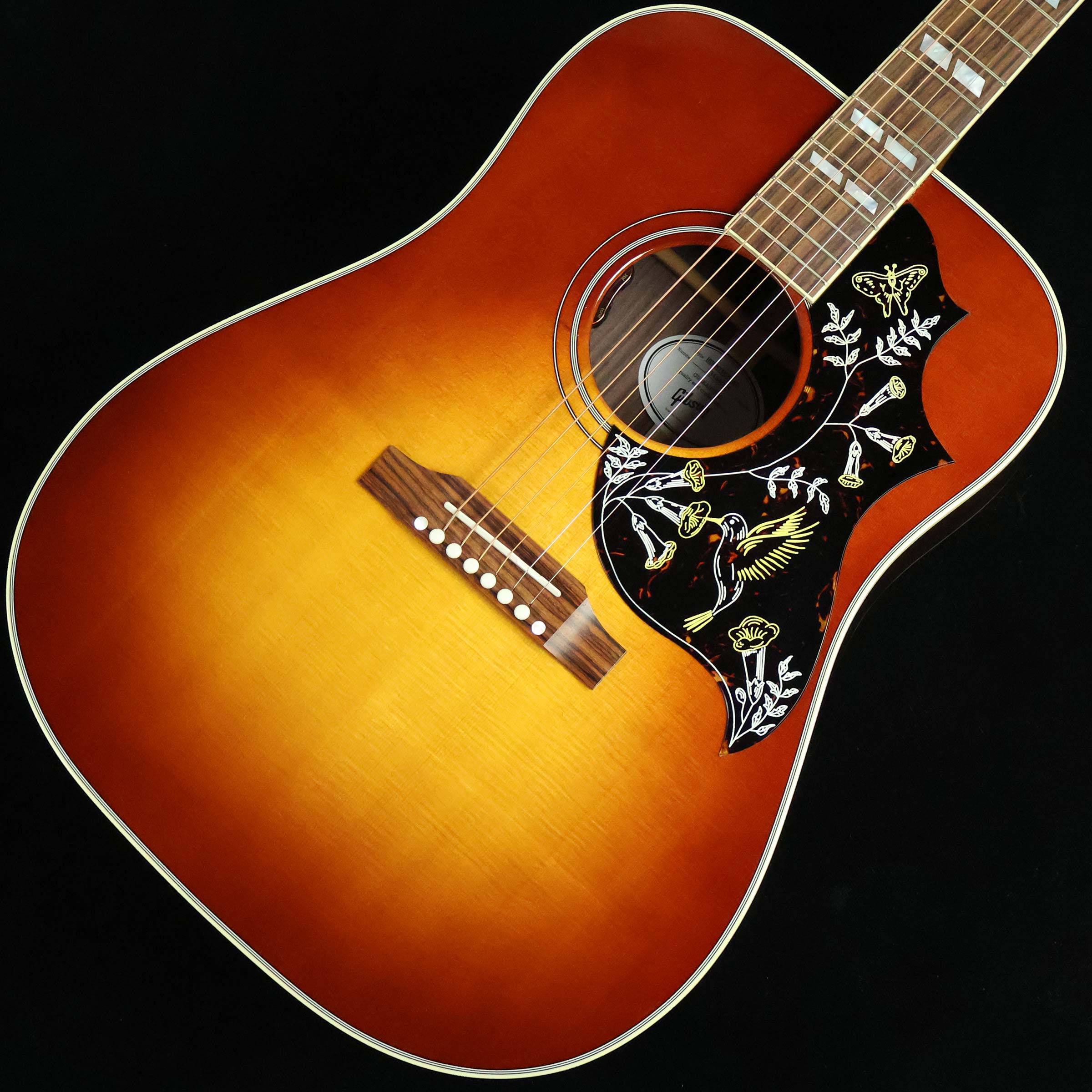華やかなルックスとダイナミックなサウンドが人気のハミングバード【特徴】1960年、「弾き語りに最適なモデル」として誕生したHummingbird。ギブソンとしてはスクエアショルダー・シェイプの第一弾でした。こちらのモデルはボディサイド&バックにローズウッドを新採用。トラディショナルなマホガニーモデルに比べて煌びやかな倍音成分と厚みのある低音域が特徴の1本となっています。ヘッドのクラウン・インレイ、指板のパラレログラム・インレイ、そして何よりもハチドリが描かれたピックガードがこのモデルの最大の特徴ですね。ピックアップはL.R.BaggsのVTCを搭載。Volumeに加えTone Controlが可能なだけでなく、オリジナルのコンプリミッターがビルトインされているため音量に関わらずバランスの取れたサウンドが得られる仕様となっています。ミュージックシーンでは特にロック・ギタリストに好まれている傾向にありますが、フォークやブルースなど、またストロークでもフィンガーピッキングでも、プレイヤーの多様な要求にしっかりと応えてフレキシブルに対応できるモデルとなっています。【杢目マニア花井のイチオシポイント！】ギブソン・アコースティックギターを代表するモデルとしてJ-45と並んで根強い人気を誇るハミングバード。こちらサイド&バックにローズウッドを採用した新仕様。マホガニーモデルとは一味違った倍音豊かで煌びやかなトーンが際立つ1本になっています。L.R.Baggsのピックアップも搭載されているため、様々なシーンで活躍してくれますよ。この商品についての詳しいお問い合わせは TEL：0570-020-025 または「お問い合わせフォーム」よりお願いします。 【花井's Profile】長野県松本市出身。三度のメシより杢（もく）が好き、自他ともに認める杢目マニア。14年間勤務していた松本店では「ギター生産量日本一」の環境を活かし地元のメーカーや工房とコラボレーションしたショップオーダーモデルなどを多数企画。ギターの製作現場にて数々の職人とミーティングを重ね木材の知識やカスタムオーダーのノウハウを蓄積。これまで培った知識と経験を活かし、彼自身がセレクト〜撮影までおこなったギターをオンラインストアに掲載中。その魅力を全国のギターファンに伝えている。【詳細情報】BODY TOP ： Sitka SpruceBODY SIDE & BACK ： RosewoodBRACING ： Traditional Hand Scalloped X-bracingNECK ： Mahogany （Round Profile）FINGERBOARD ： Indian RosewoodINLAY ： Mother of Pearl ParallelogramNUT ： TUSQ（43.81mm）BRIDGE ： RosewoodTUNER ： Grover RotomaticSTRINGS ： .012 - .053PICKUP ： L.R.Baggs VTCCONTROLS ： 1Vol、1ToneCOLOR ： Rosewood BurstCASE ： HardcaseJANコード：0711106146973【gibson】【gbsnmkm_kw】