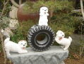 全部石彫刻品でできた台付きタイヤに乗った３匹の犬【ガーデニングオーナメント】