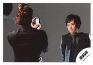 【中古】生写真(ジャニーズ)/アイドル/嵐 嵐/二宮和也/横型・上半身・衣装黒・ネクタイ・目線左・手前に人・カメラ・背景グレー/公式生写真